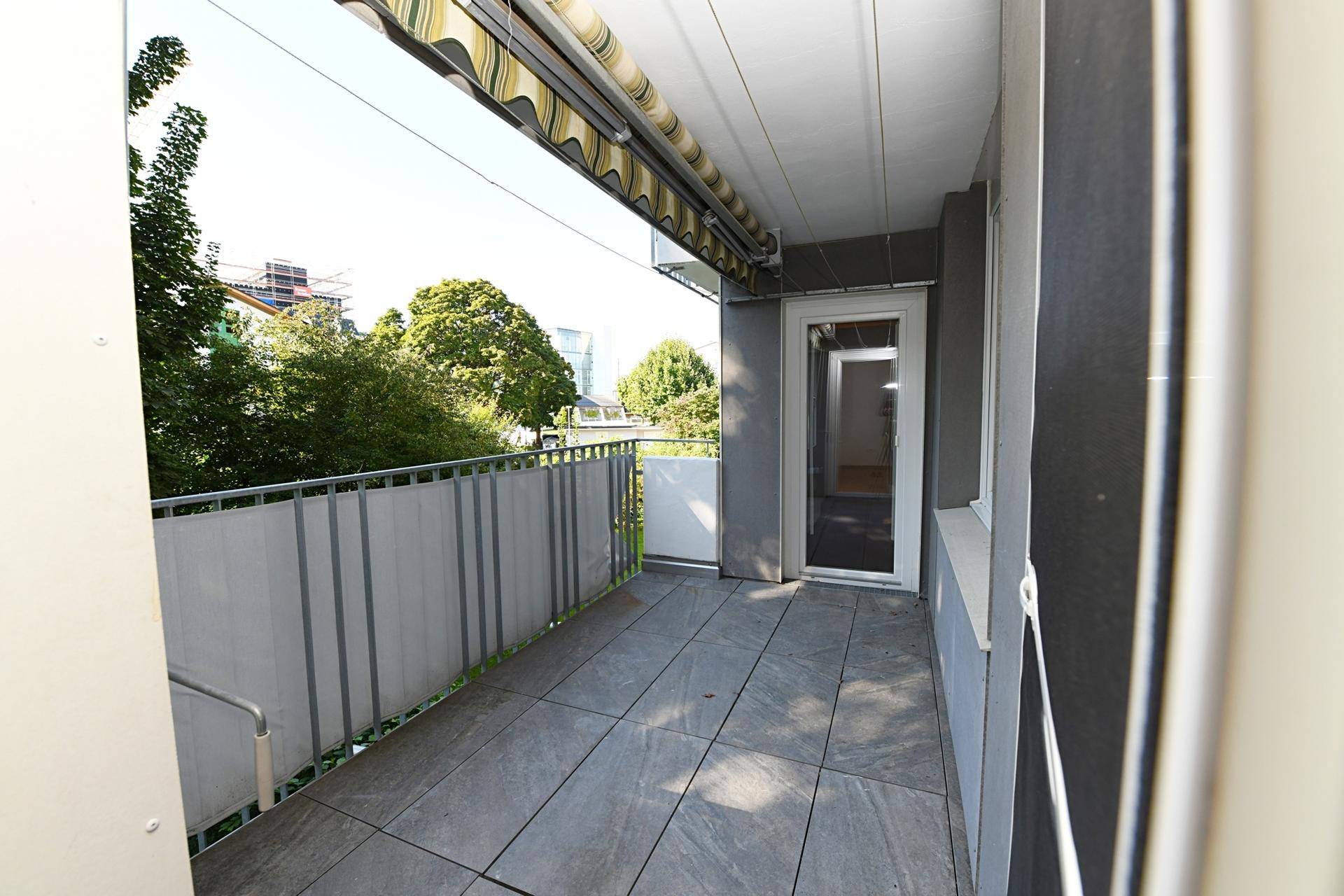 Geräumiger Balkon mit Fliesenboden, Markise und weitem Blick ins Grüne.