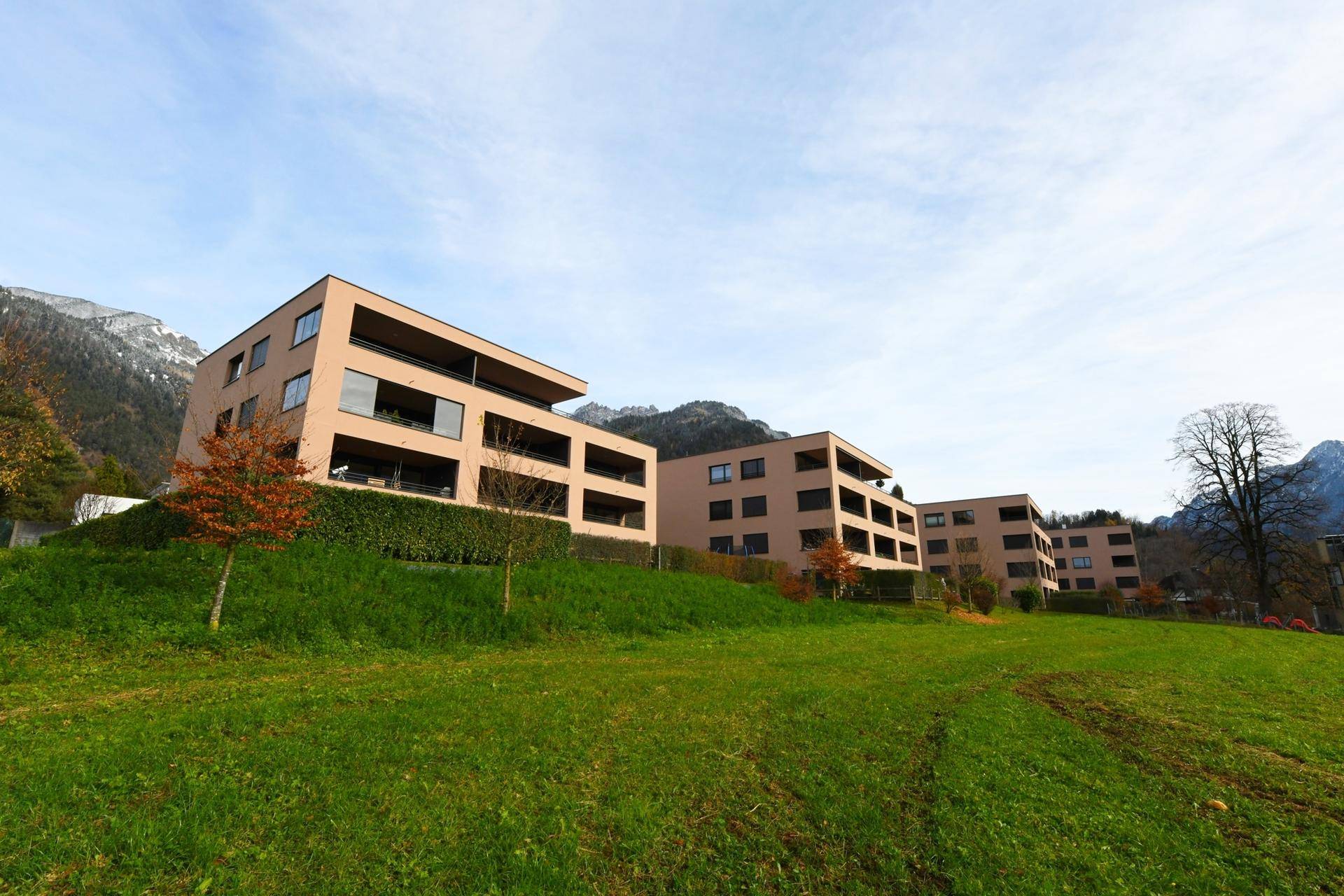 Moderne Wohngebäude auf einem grünen Hügel mit Bergblick im Hintergrund.