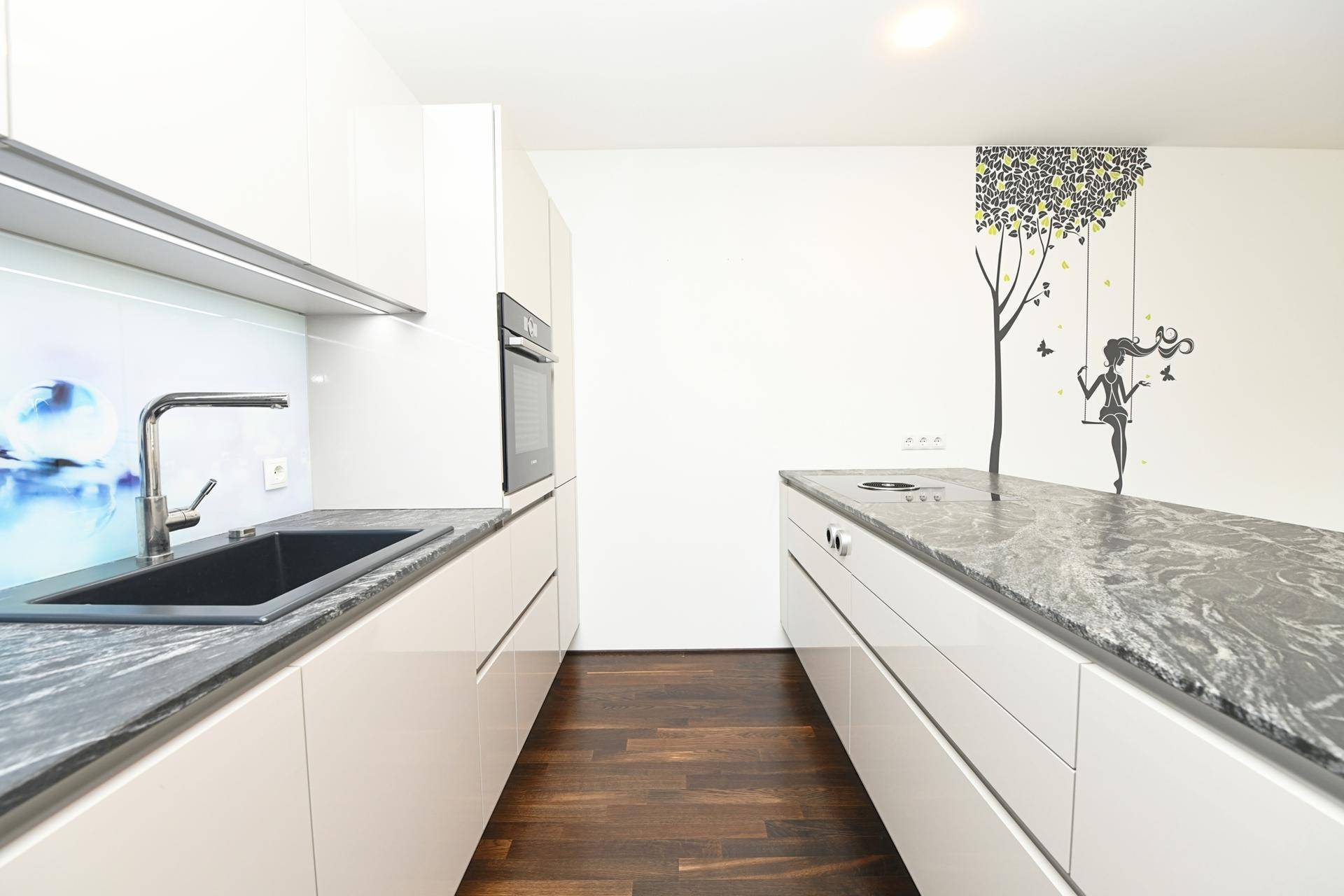 Schlanke, moderne Küche mit weißen Schränken, Granitplatten und Holzboden.