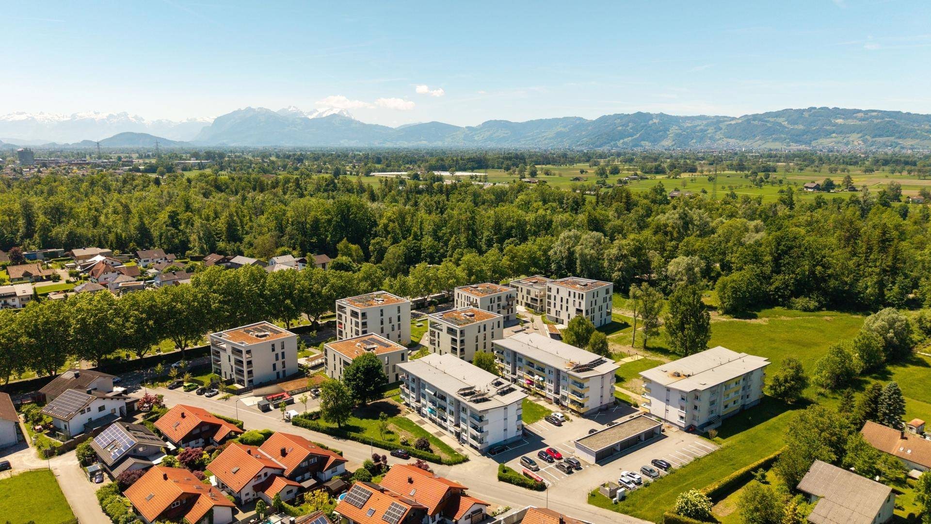 Panoramablick aus der Luft auf eine Wohnsiedlung mit Bergen im Hintergrund.