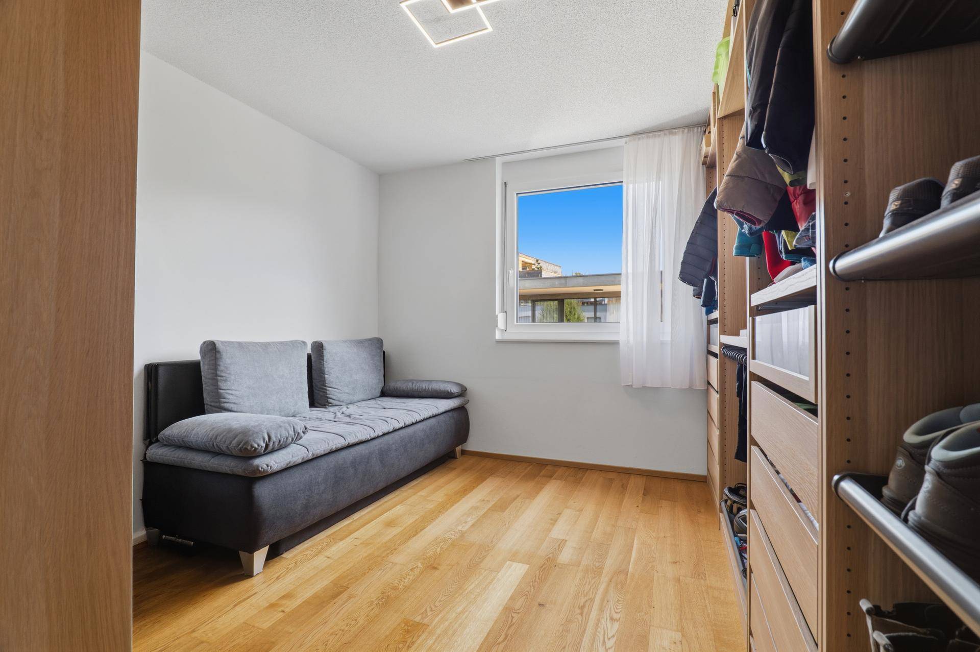 Zimmer mit Holzboden, Sofa und integrierten Regalen für Kleidung und Schuhe.