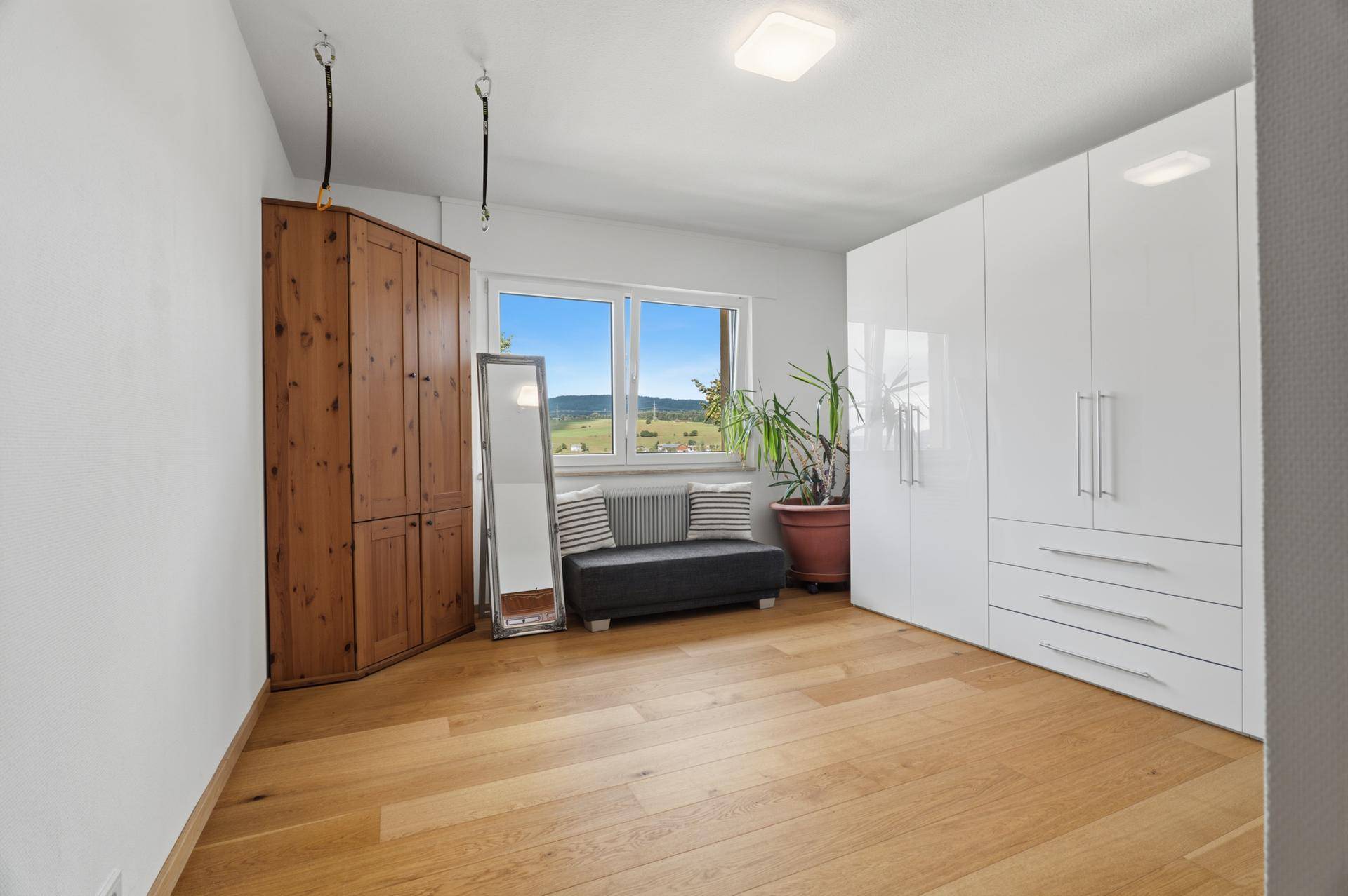 Geräumiges Schlafzimmer mit Parkettboden, weißen Kleiderschränken und Blick ins Grüne.