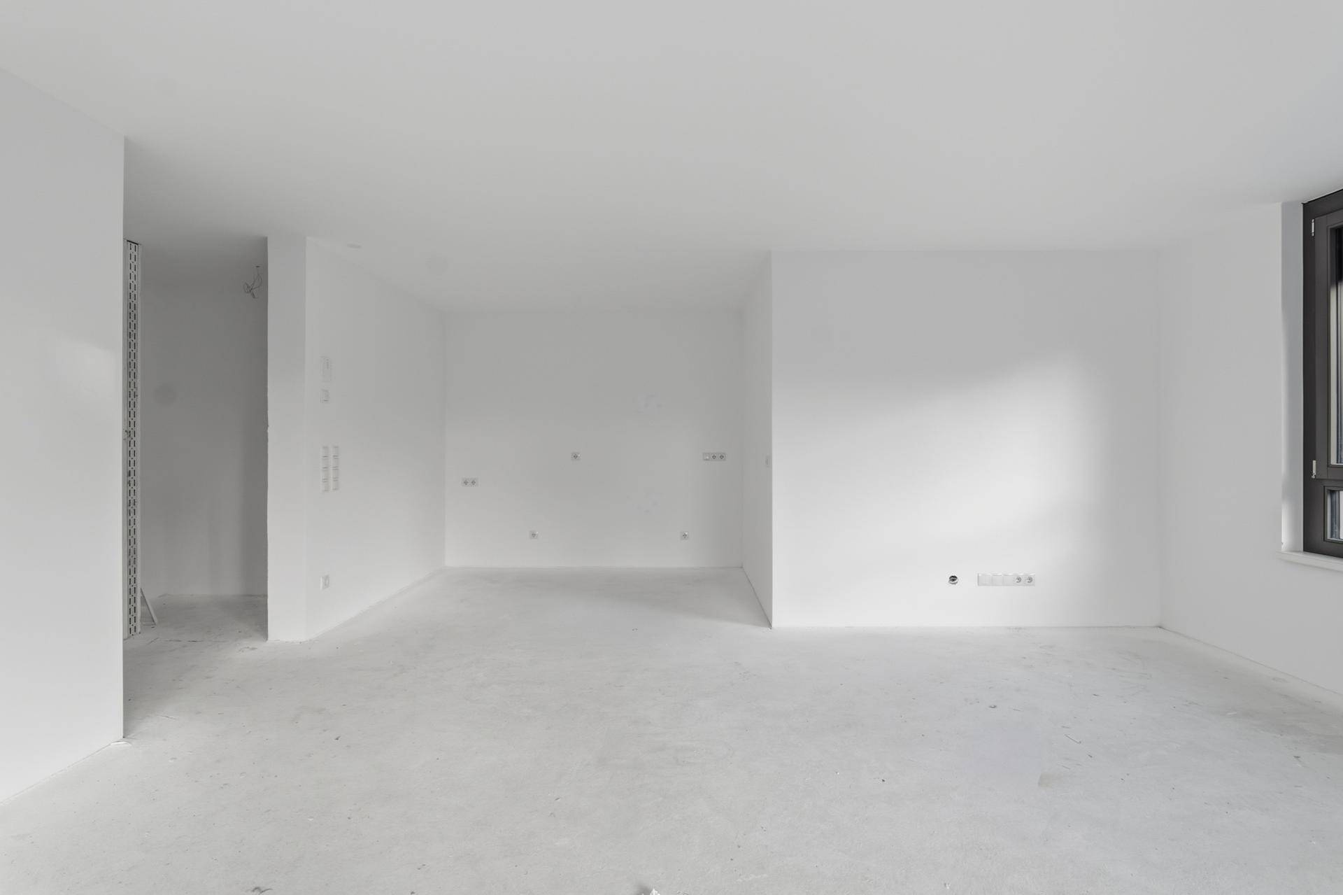 Heller, unmöblierter Wohnraum mit großen Fenstern und viel Tageslicht.
