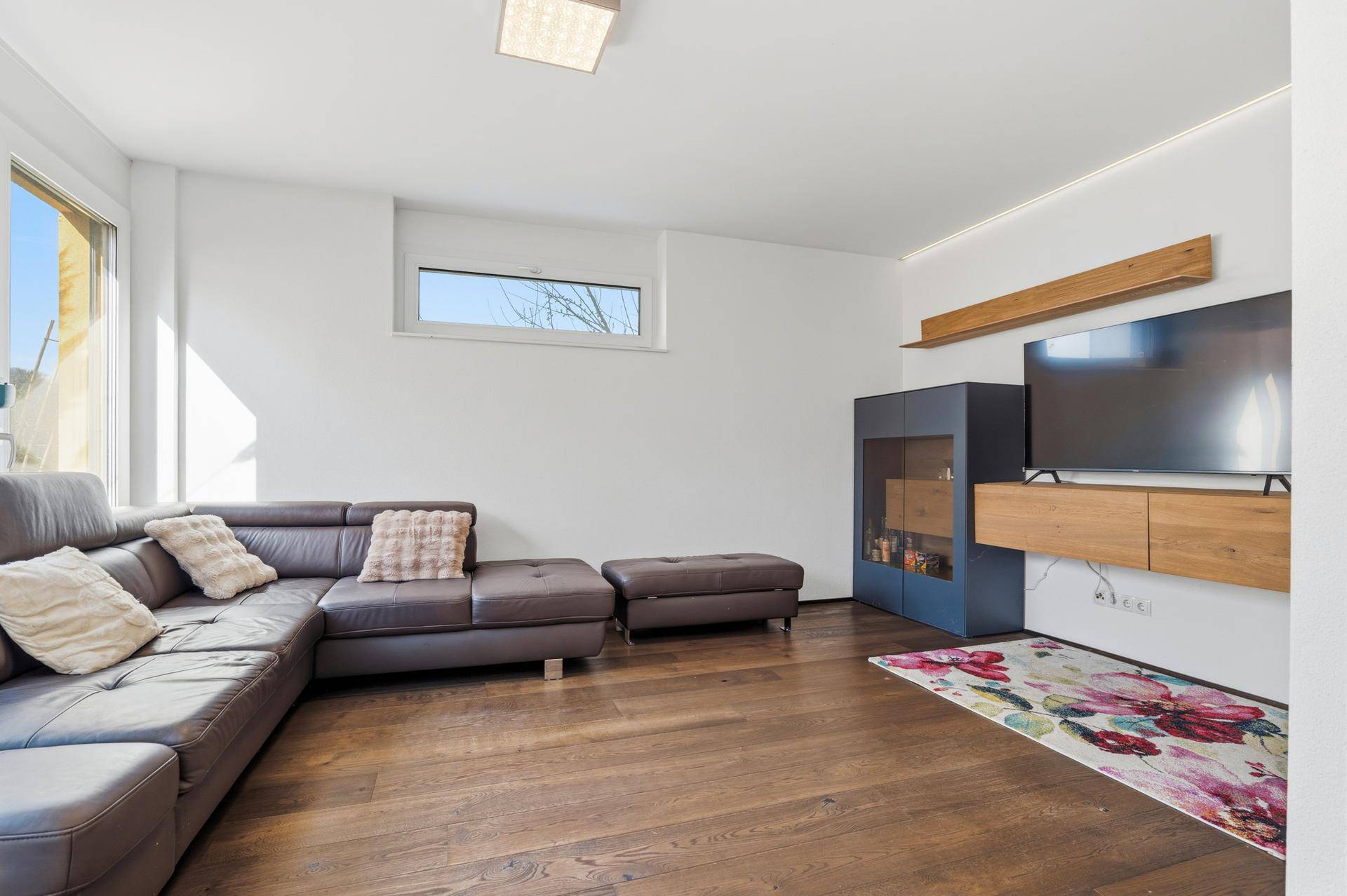 Gemütliches Wohnzimmer mit Ledersofa, Holzboden und großem Fernseher.