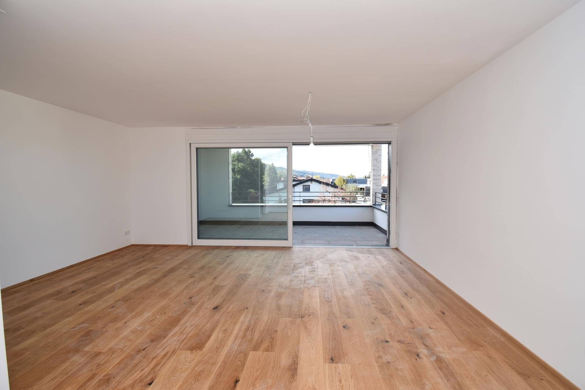 Geräumiger Wohnbereich mit Zugang zu einem großen Balkon und weitem Blick ins Grüne.