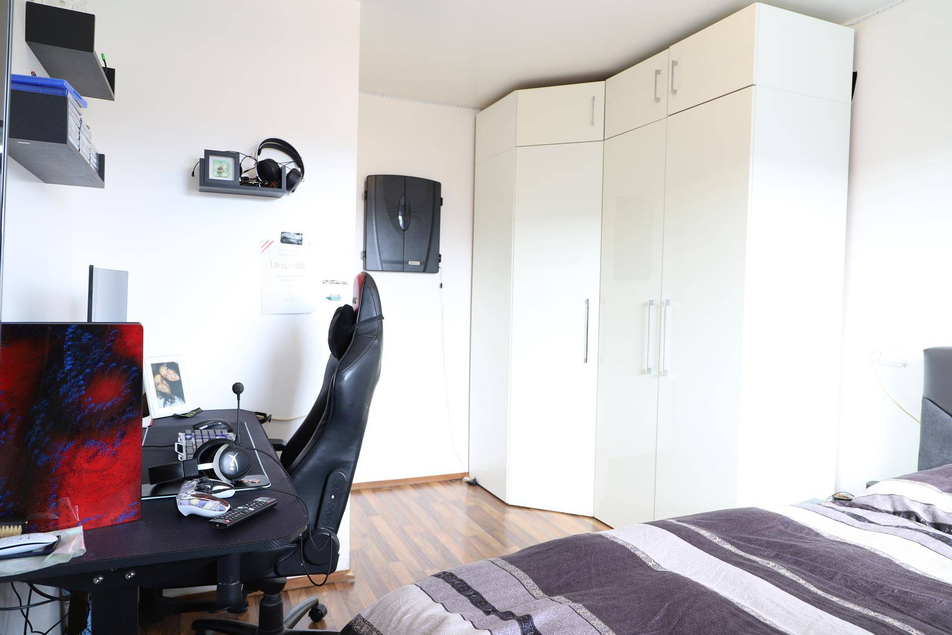 Helles Schlafzimmer mit Holzboden, weißem Eckschrank und modernem Arbeitsbereich.