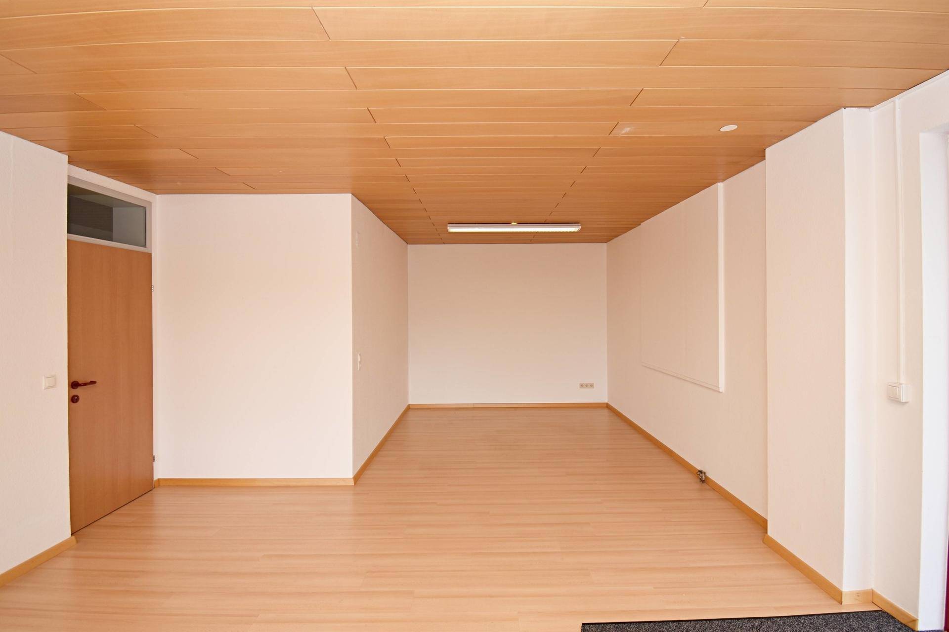 Leerer, heller Büroraum mit Laminatboden und Holzdecke, ideal für verschiedene Nutzungen.