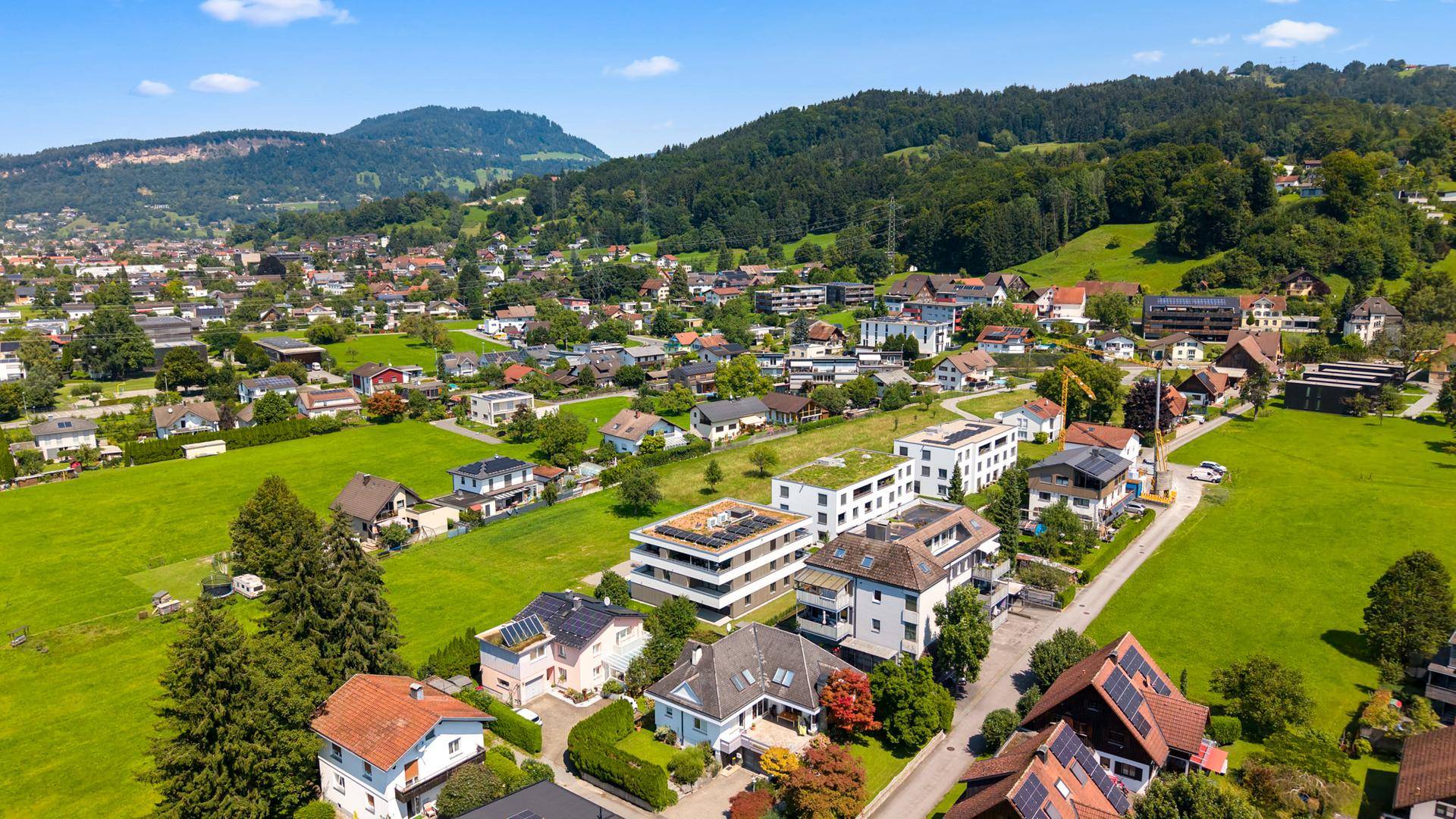 Weitläufige Luftaufnahme einer Wohngegend mit grünen Hügeln und moderner Architektur.