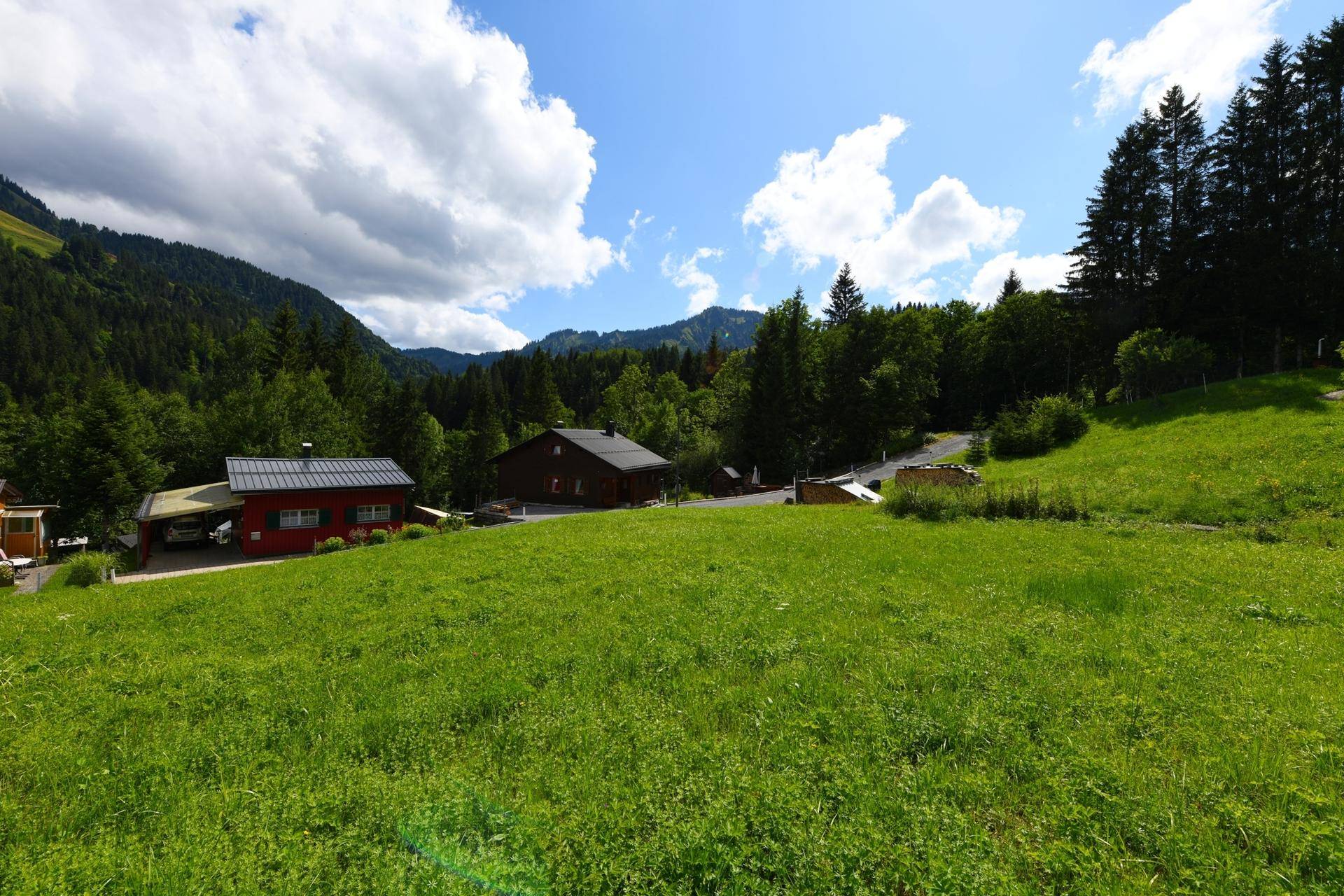 Sonnige grüne Wiese mit Blick auf charmante Häuser und die umliegende Berglandschaft.