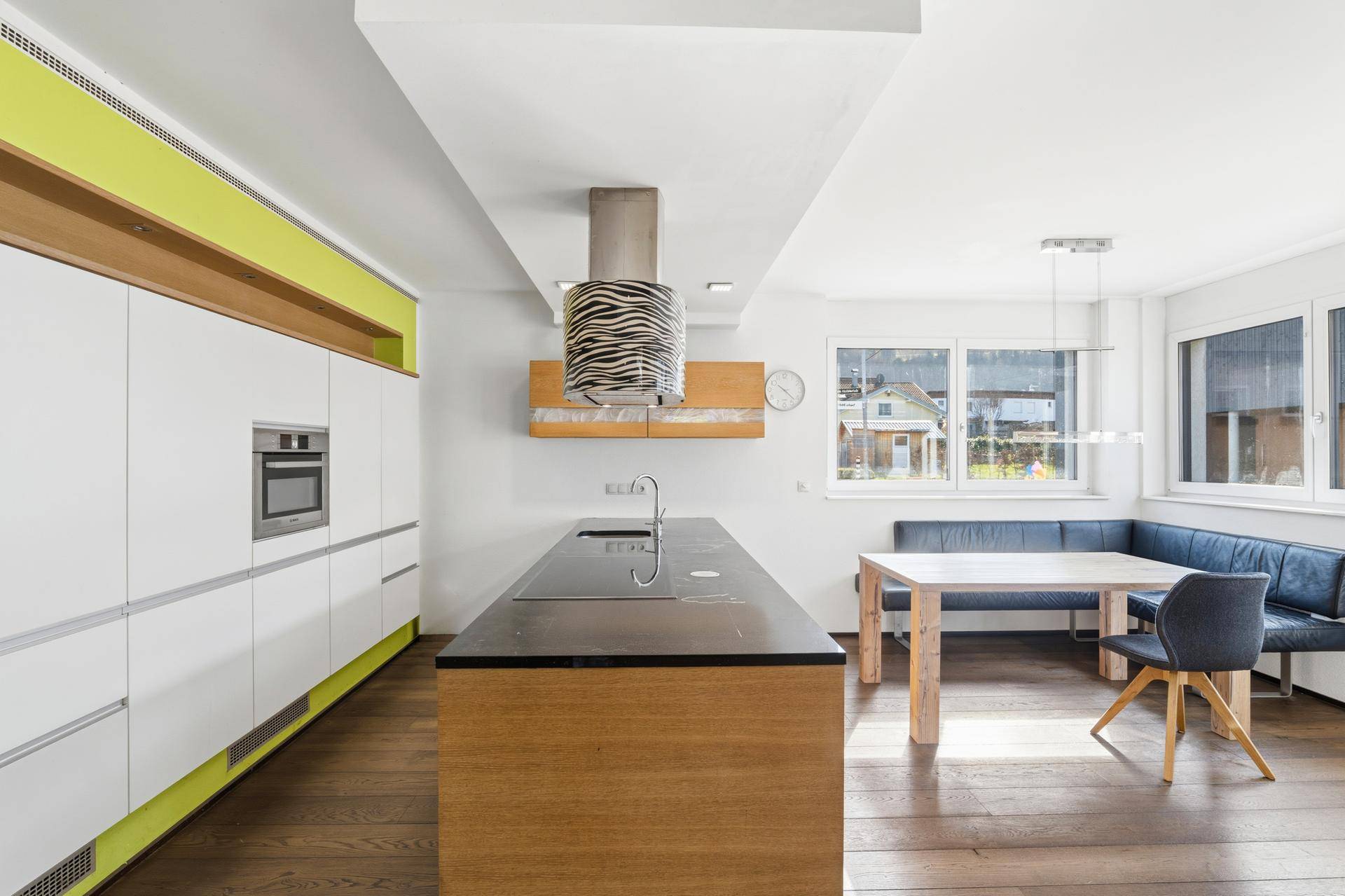 Moderne Küche mit Kochinsel, Holzboden und integriertem Essbereich mit Sitzbank.