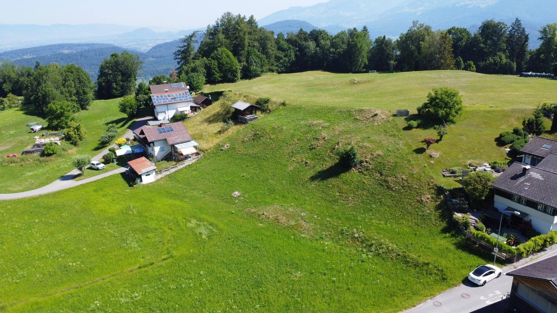 Weitläufige Luftaufnahme eines grünen Grundstücks mit umliegenden Häusern und Bergsicht.