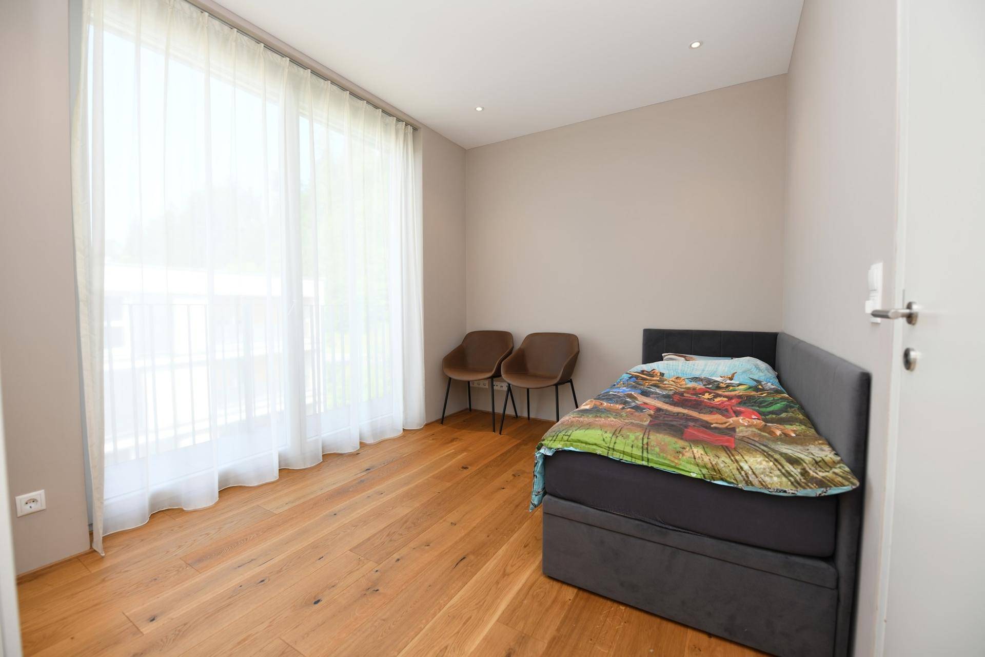 Helles Schlafzimmer mit Holzboden, großem Fenster und Einzelbett.