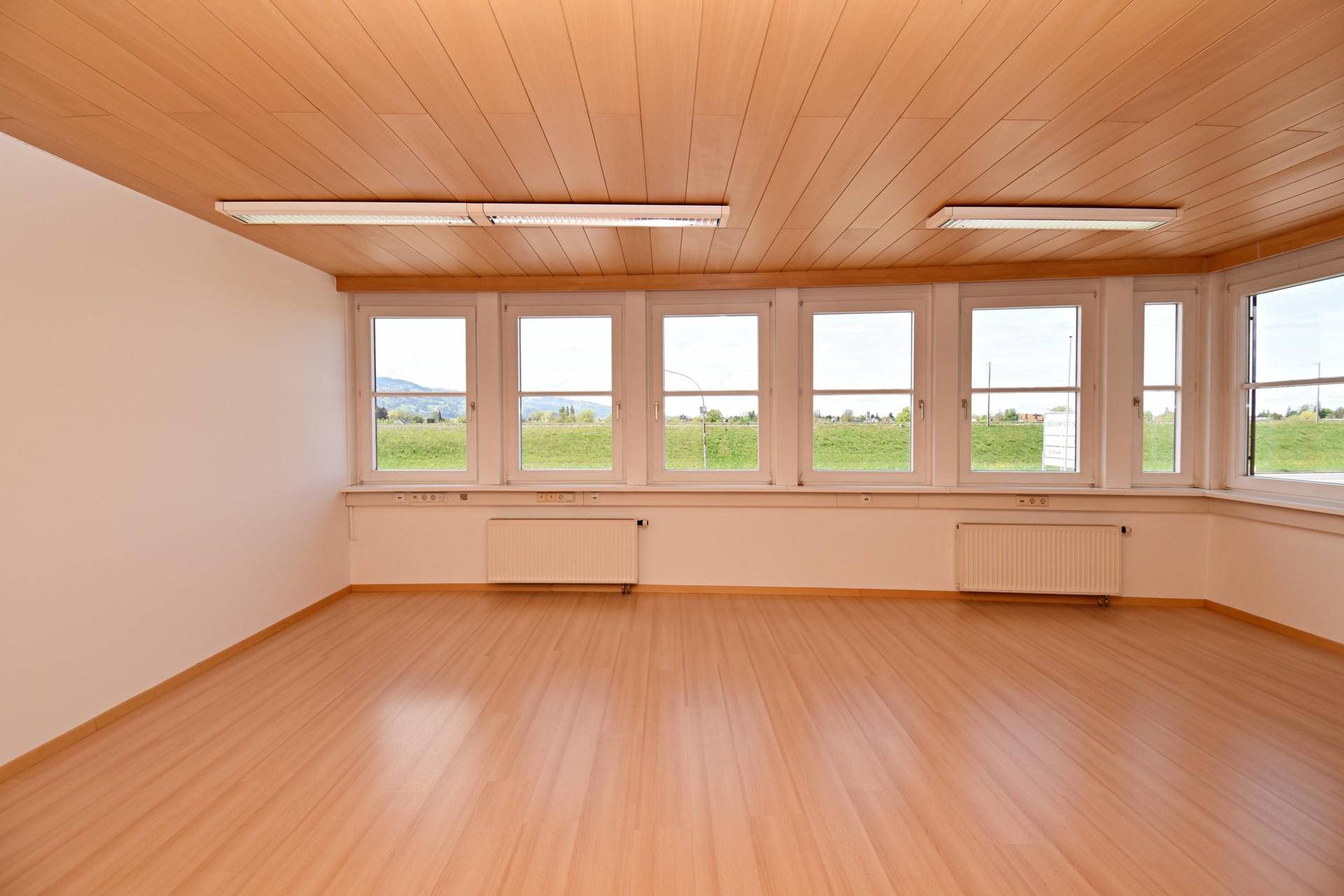 Großes, helles Büro mit vielen Fenstern, Laminatboden und Holzdecke, ideal für Teamarbeit.