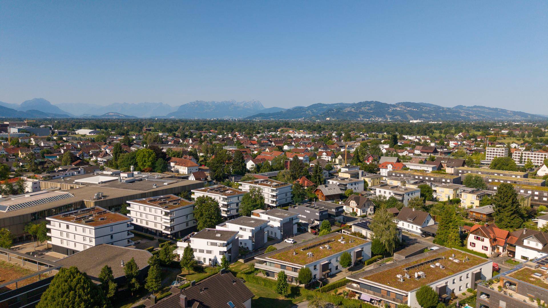 Weitläufige Luftaufnahme einer Wohngegend mit vielen Grünflächen und Bergsicht.