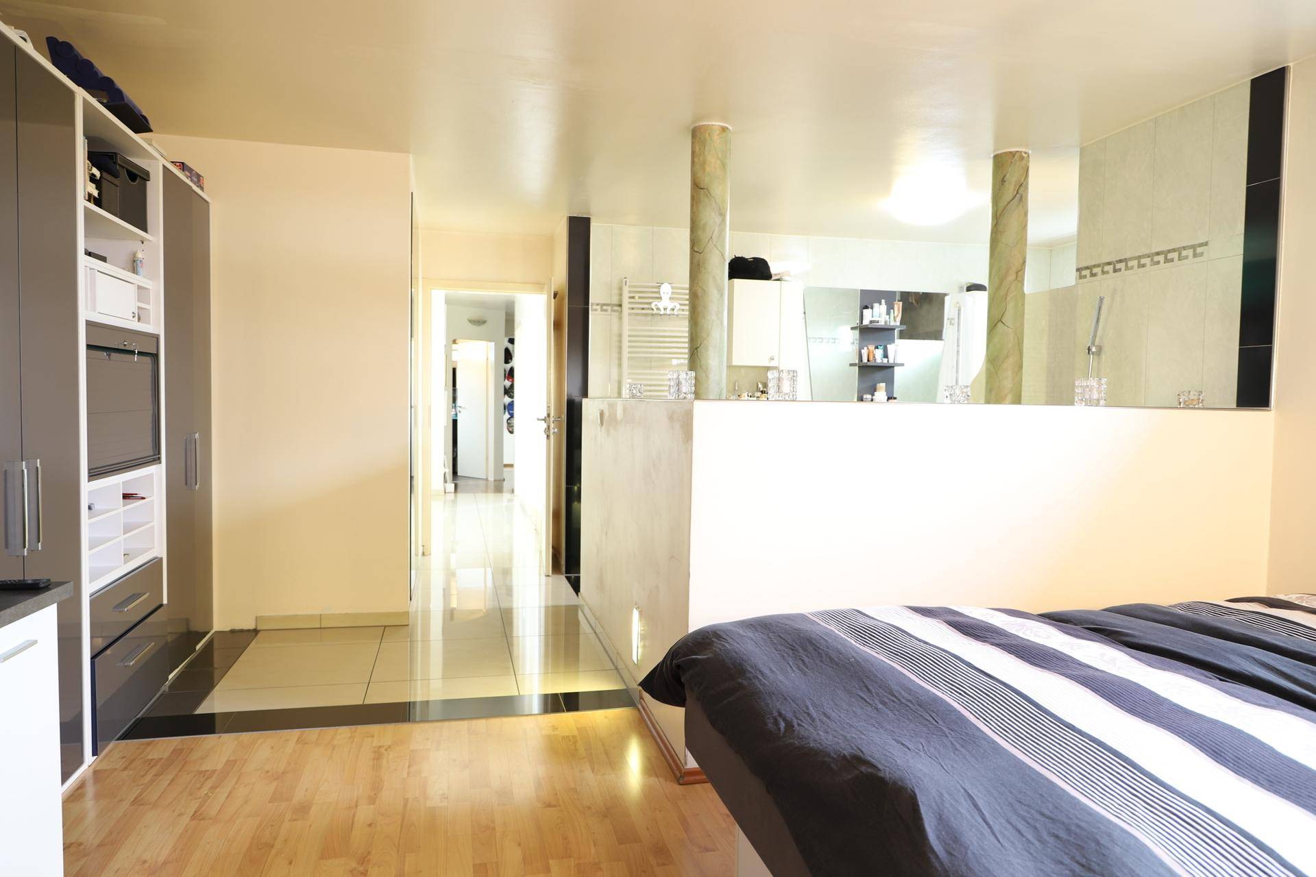 Schlafzimmer mit integriertem Badbereich, Holzboden und modernen Einbauschränken.
