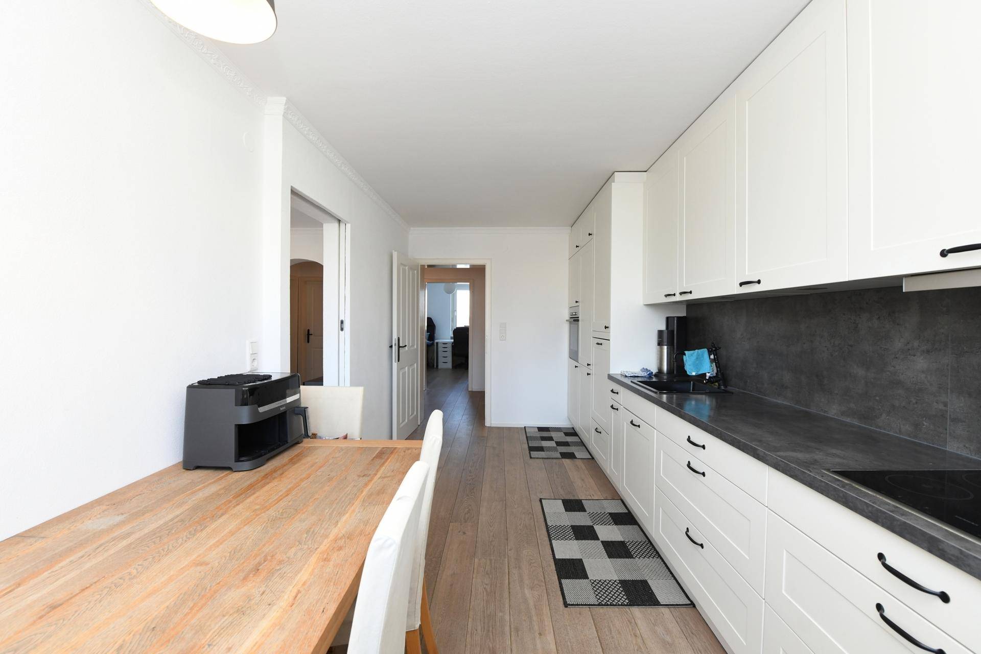 Funktionale Küche mit Essbereich, Holzboden und Blick in den Flur.