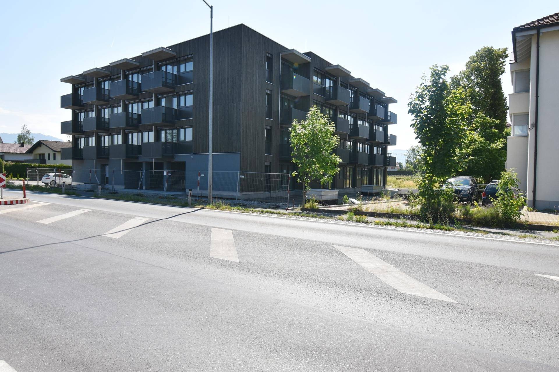 Neubau mit zeitgenössischer Architektur, dunkler Fassade und mehreren Balkonen an der Straße.