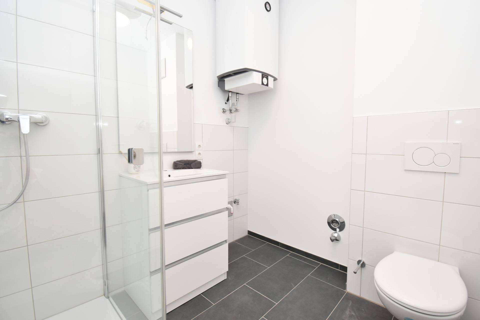 Modernes Badezimmer mit Dusche, WC und Waschbeckenunterschrank in Weiß und dunklen Fliesen.