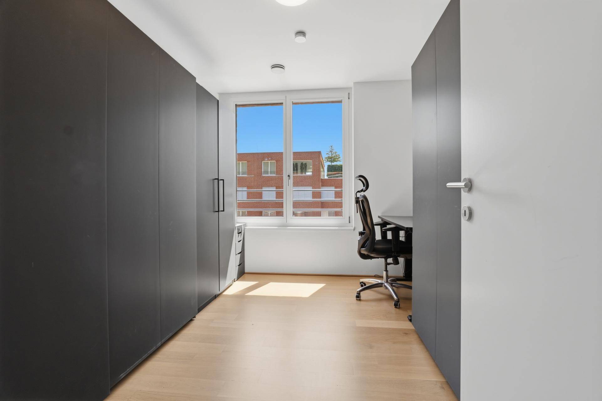 Funktionaler Raum mit Einbauschränken, Schreibtisch und Fenster, ideal als Büro oder Ankleidezimmer.