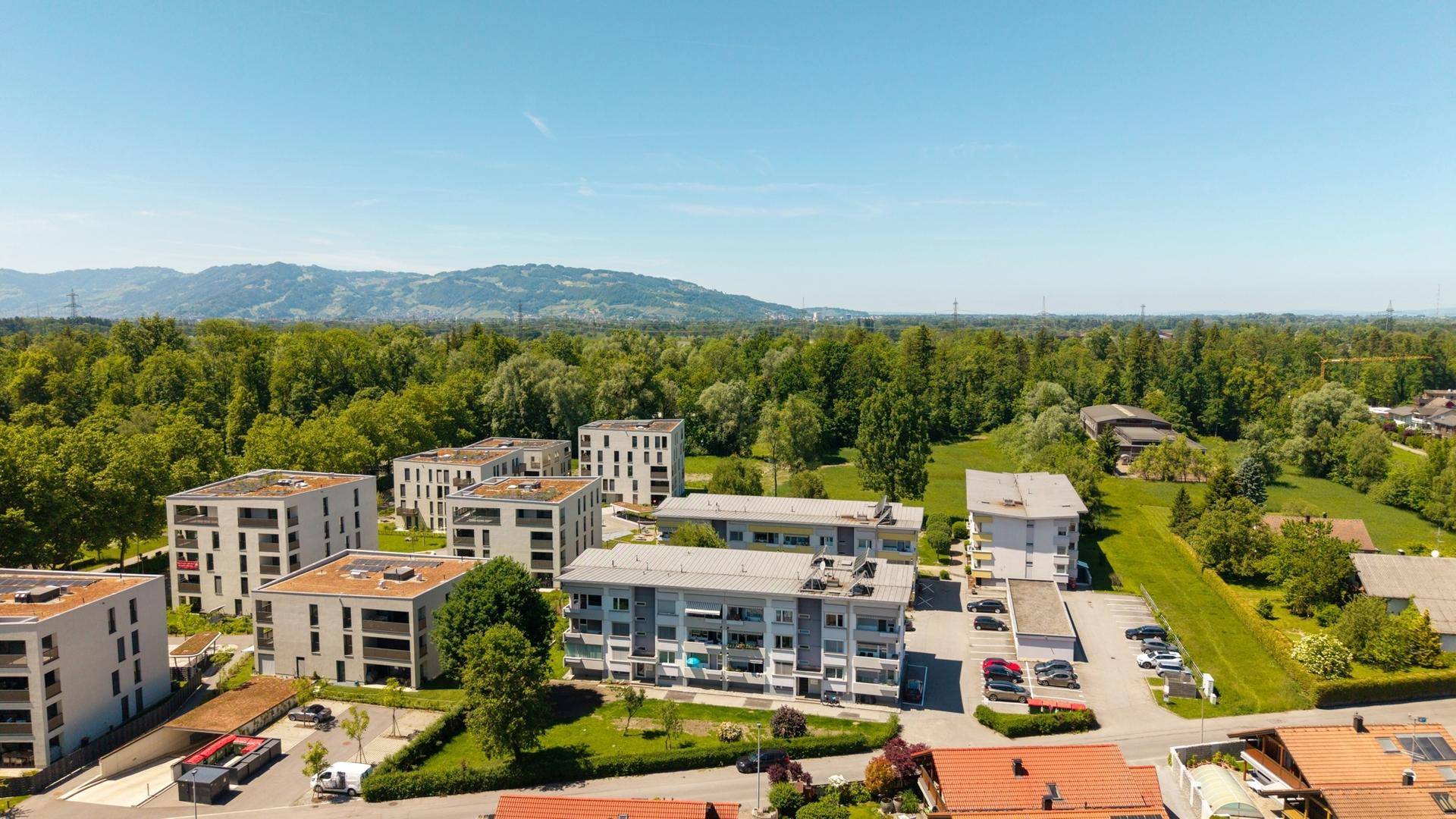 Weitläufige Luftaufnahme einer Wohnsiedlung umgeben von Wäldern und Bergen.