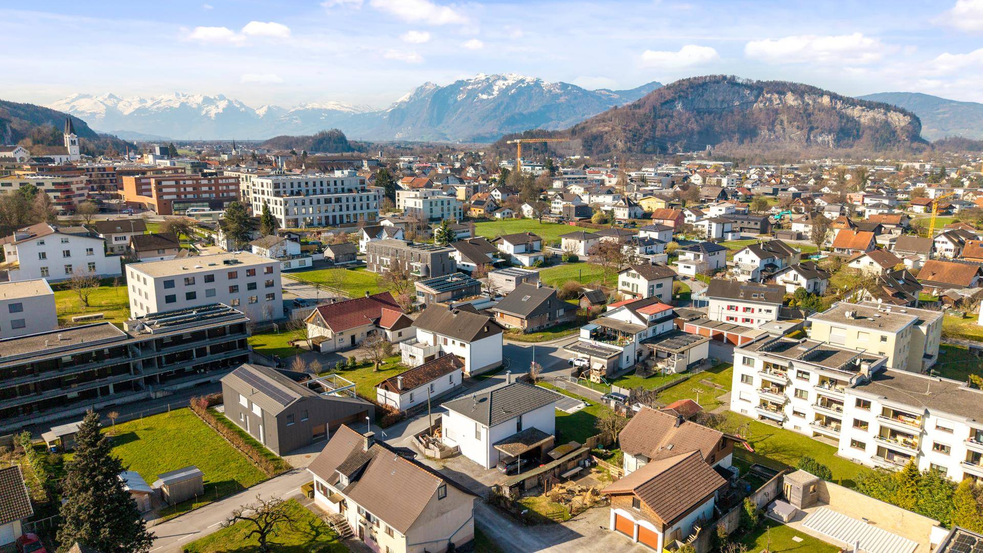 Weitläufige Luftaufnahme einer Stadt mit Wohngebieten und Bergpanorama.