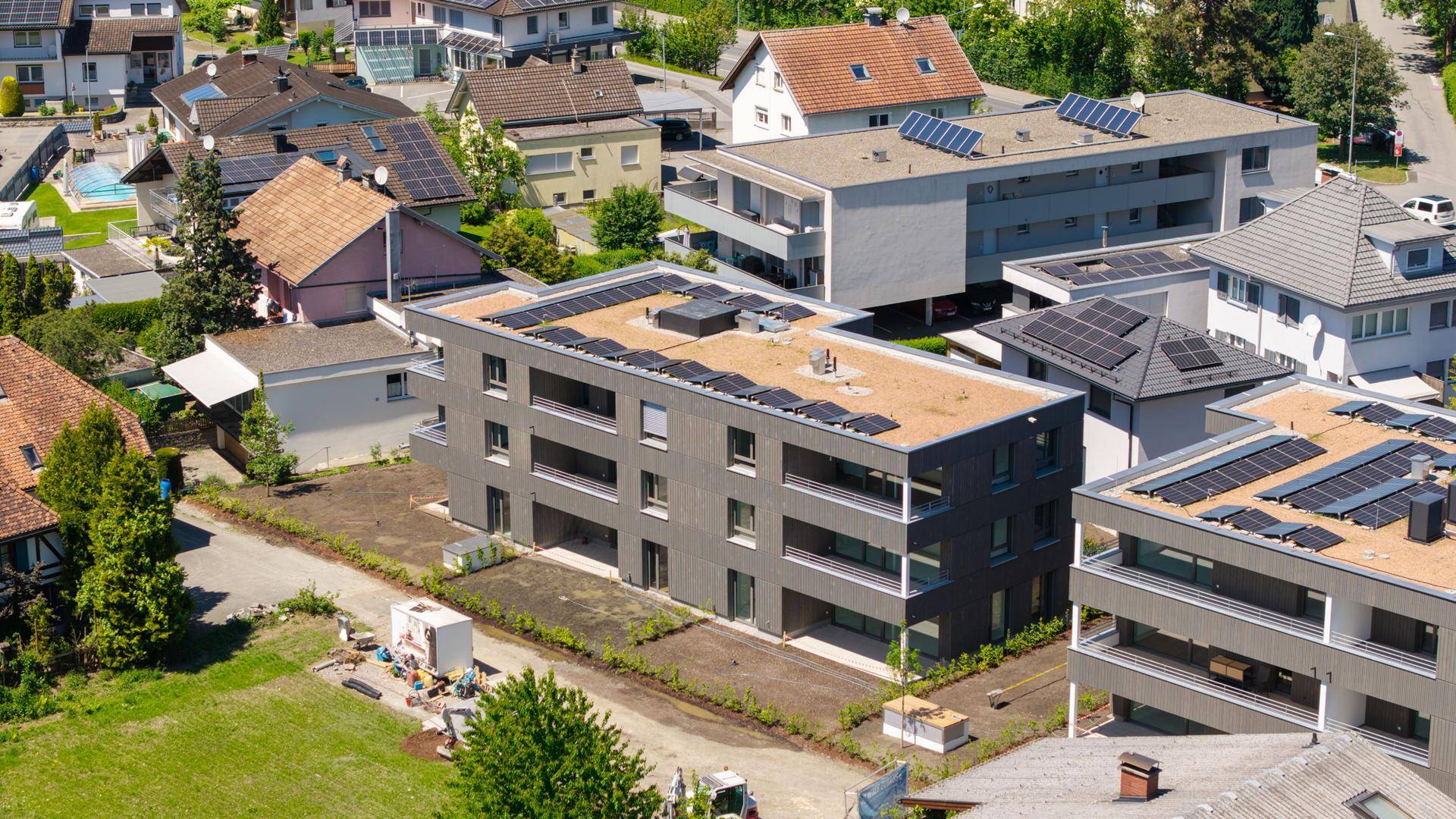 Luftaufnahme von modernen Wohngebäuden mit Flachdächern und Solaranlagen, umgeben von anderen Häusern.