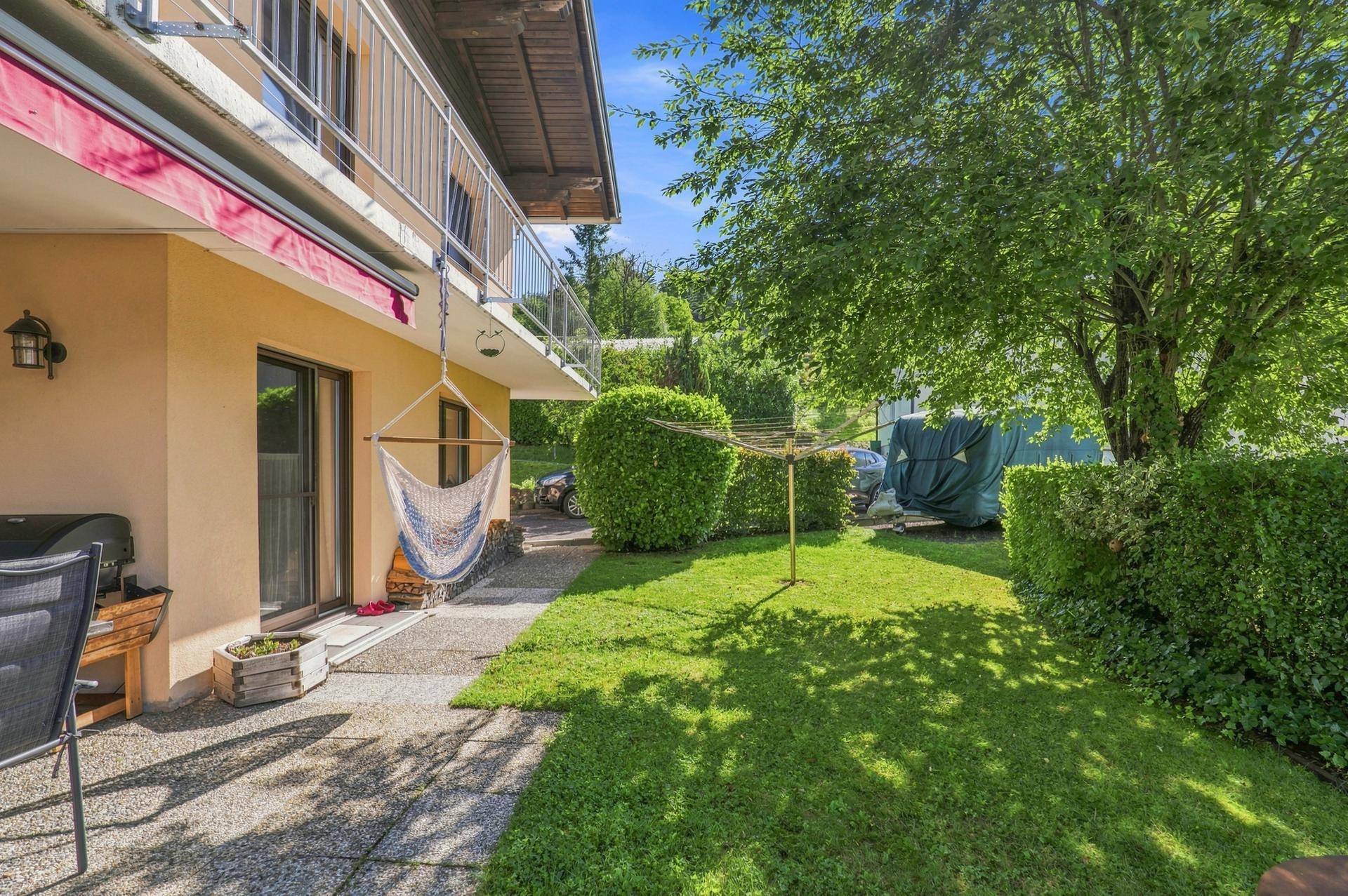 Grüner Gartenbereich mit Hängematte, Wäschespinne und Zugang zu einer kleinen Terrasse.