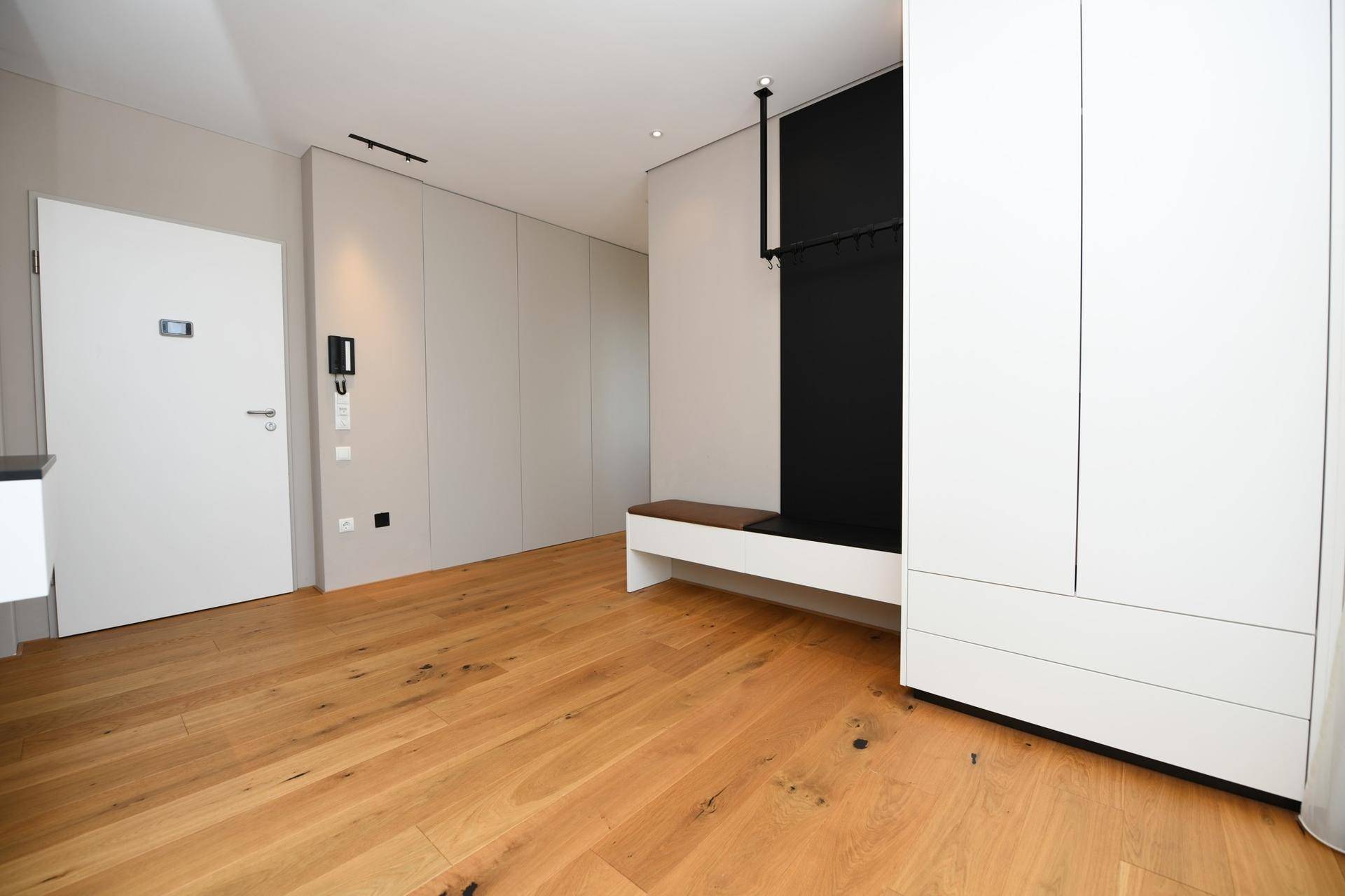 Moderner Eingangsbereich mit Holzboden, weißer Tür und integrierter Garderobe.