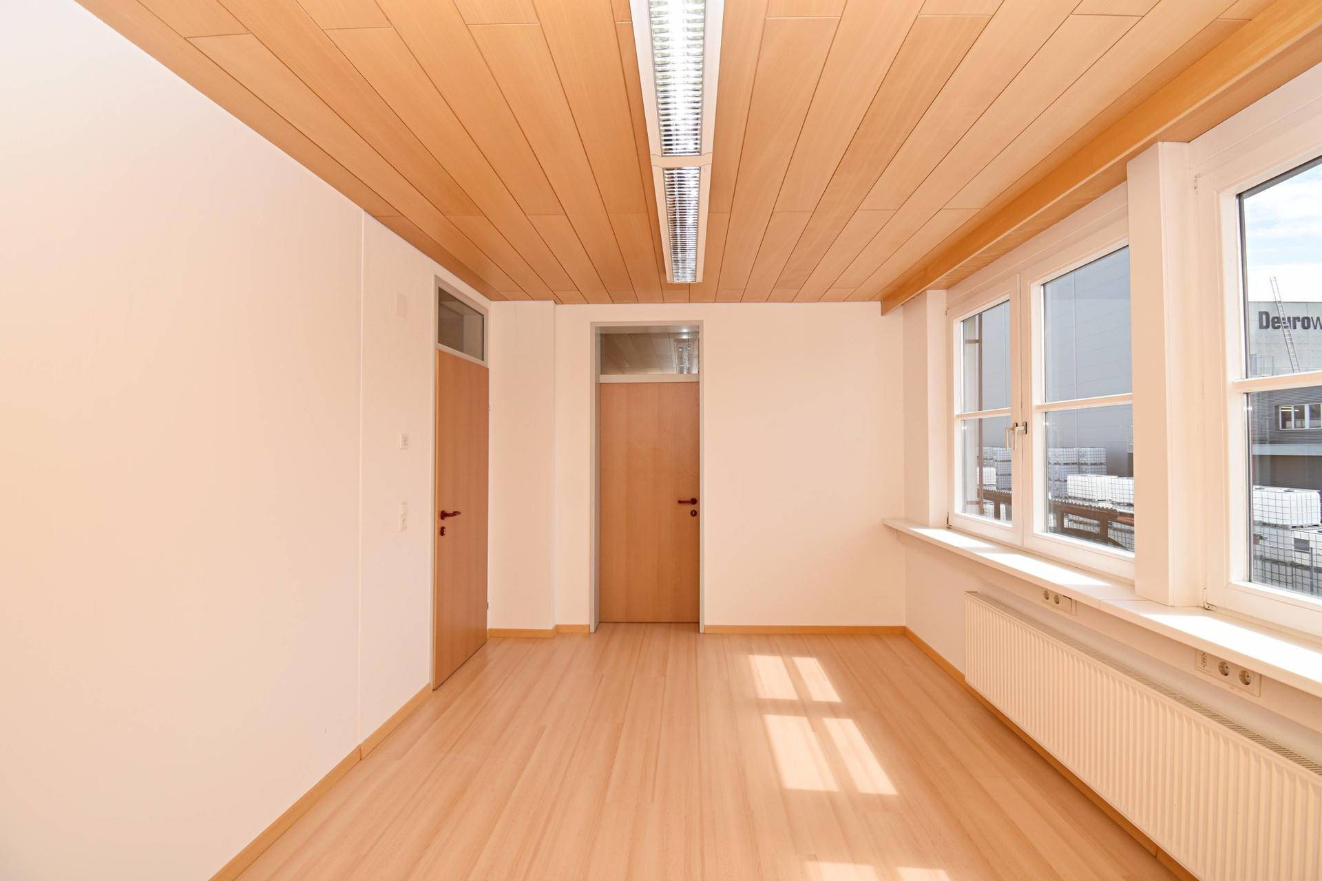 Geräumiges, helles Büro mit Laminatboden, Holzdecke und mehreren Fenstern.