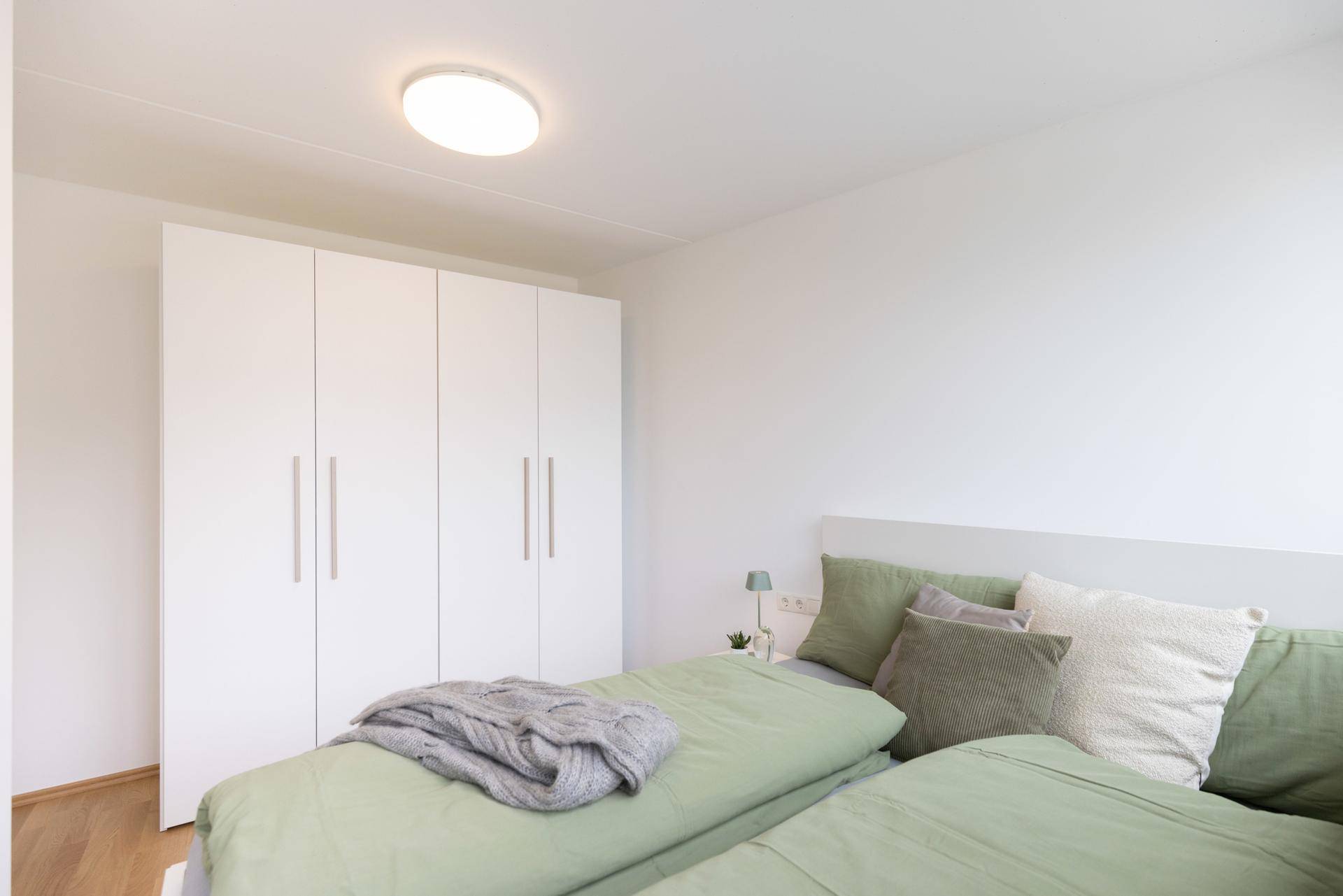 Helles Schlafzimmer mit Doppelbett, grüner Bettwäsche und einem großen weißen Einbauschrank.