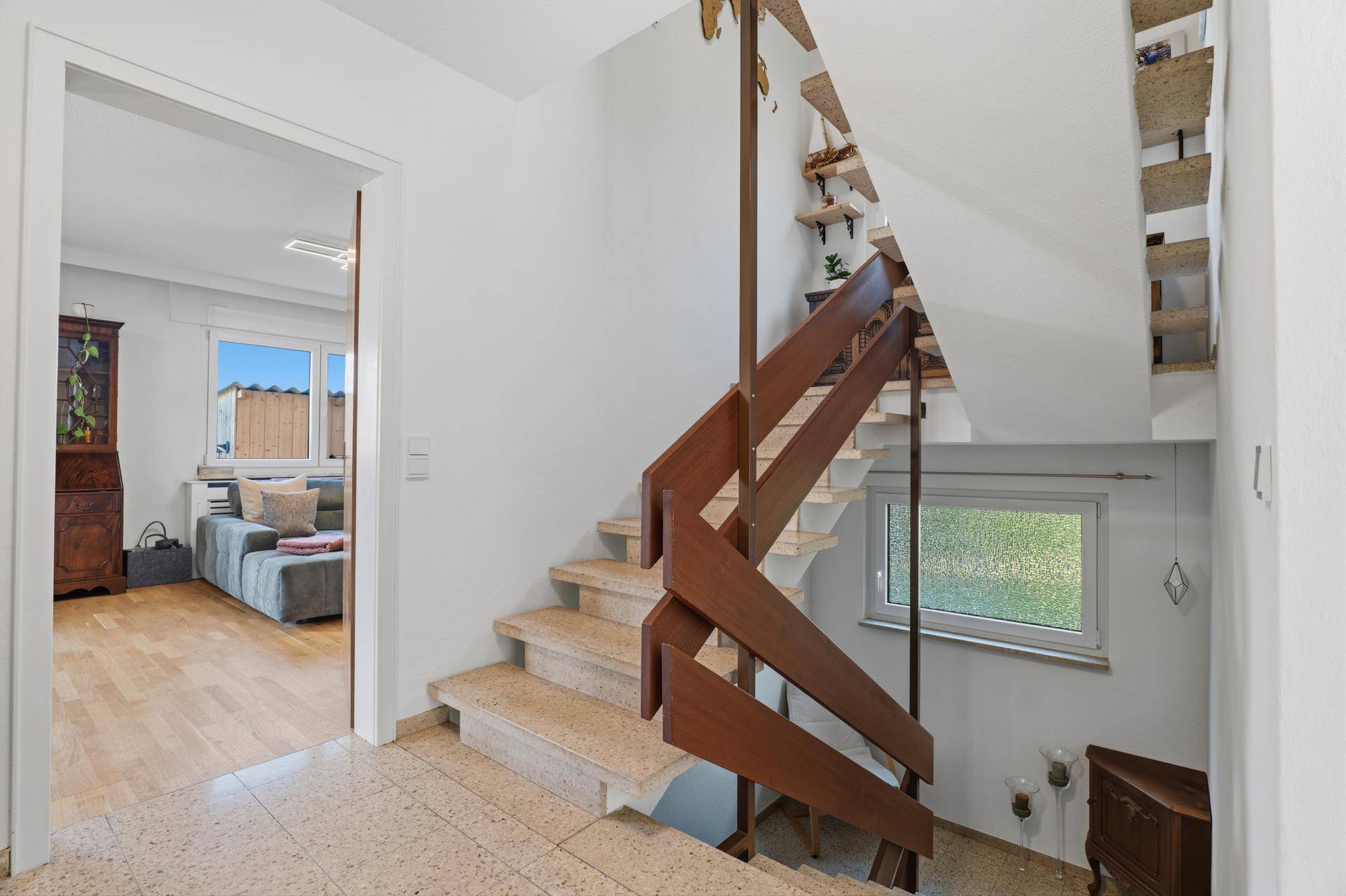 Treppenhaus mit Holzgeländer und Terrazzostufen, das zu den Wohnbereichen führt.