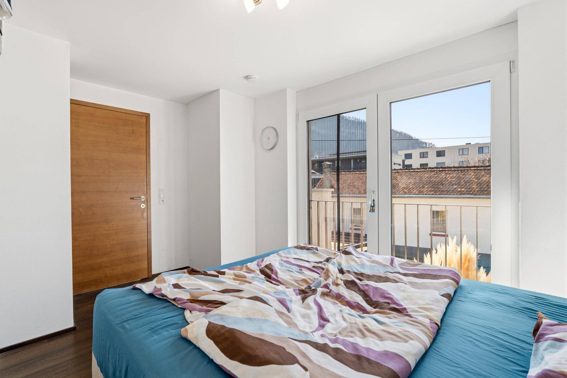 Schlafzimmer mit Holzboden und Blick auf die Umgebung durch die Balkontür.