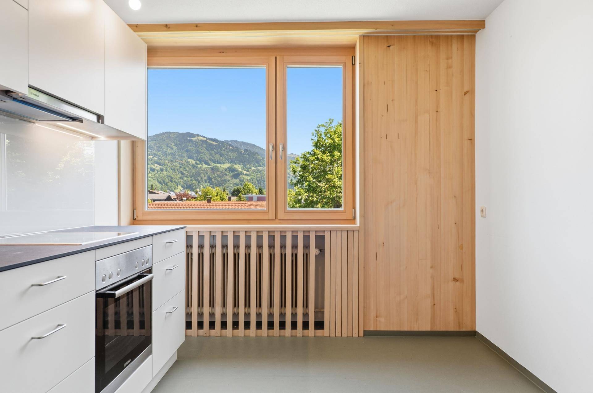 Helle Küche mit Fensterblick auf grüne Berge und Holzverkleidung an der Wand.