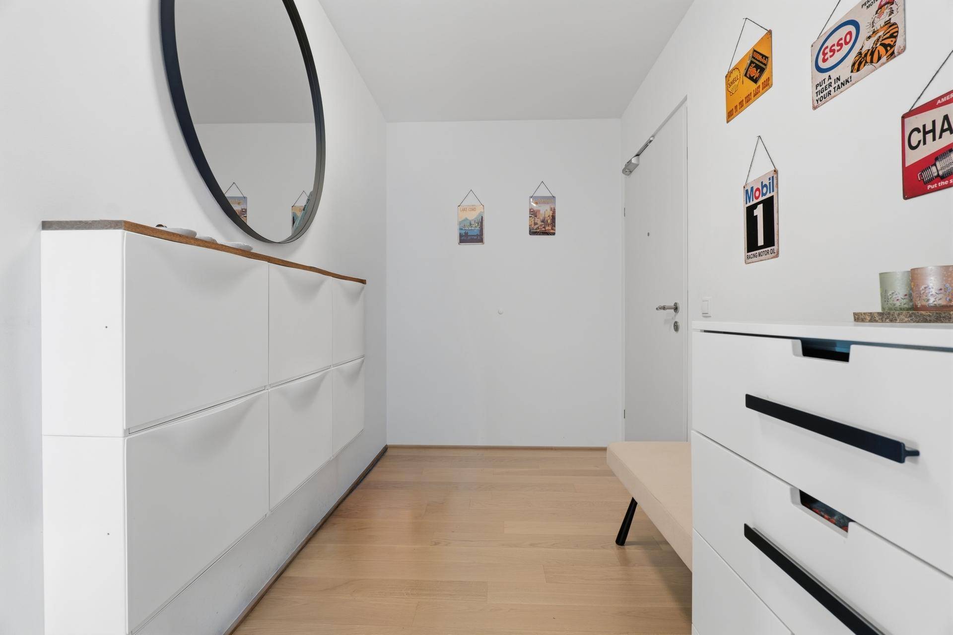 Heller Eingangsbereich mit rundem Spiegel, Schuhschrank und kleiner Sitzgelegenheit.