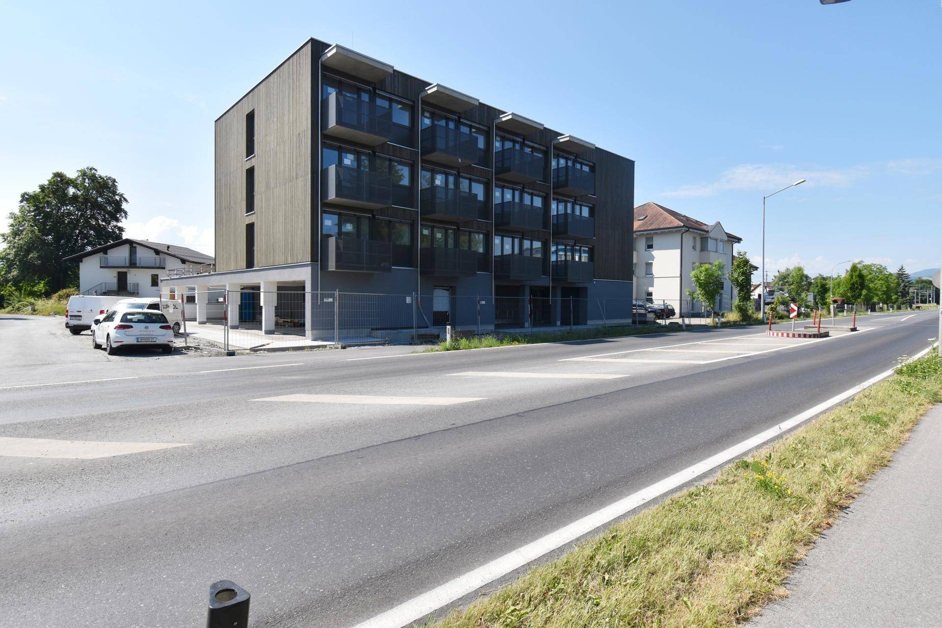 Modernes Mehrfamilienhaus mit dunkler Holzfassade und Balkonen an einer Straße gelegen.