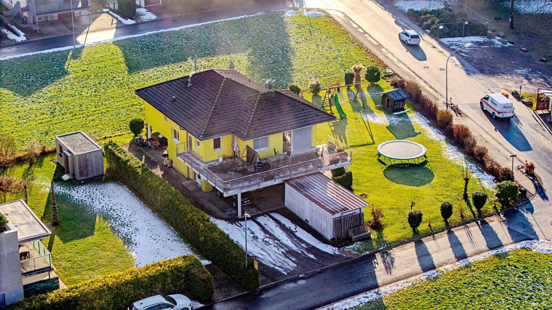 Luftaufnahme des gelben Einfamilienhauses mit Garten und umliegender Bebauung.