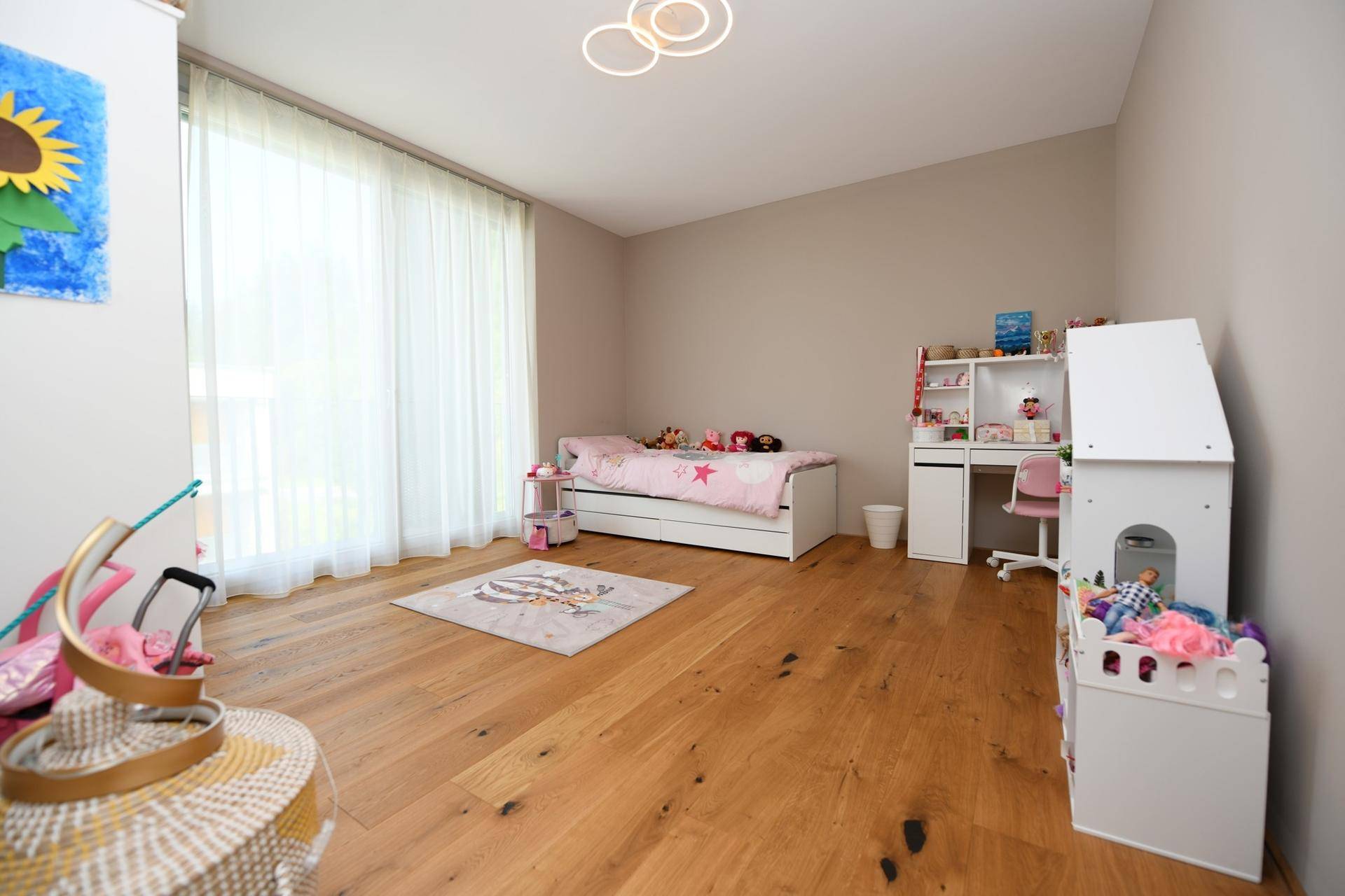 Kinderzimmer mit Holzboden, großem Fenster und verspielter Dekoration.