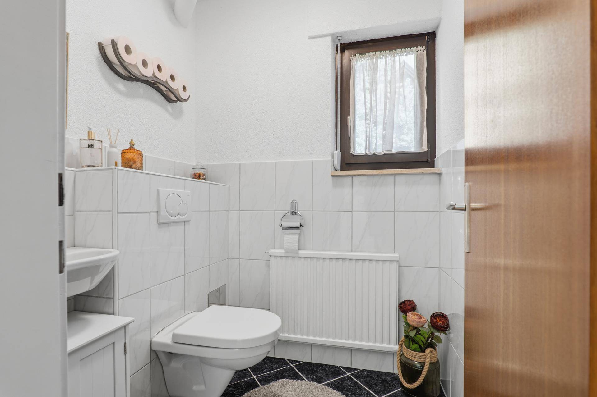 Kleines Gäste-WC mit Fenster, Waschbecken und Wand-WC.