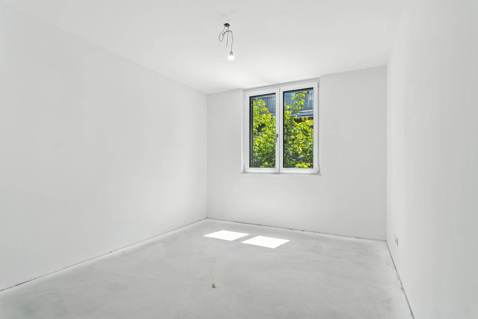 Unmöblierter Raum im Rohbau mit Blick ins Grüne und viel natürlichem Licht.