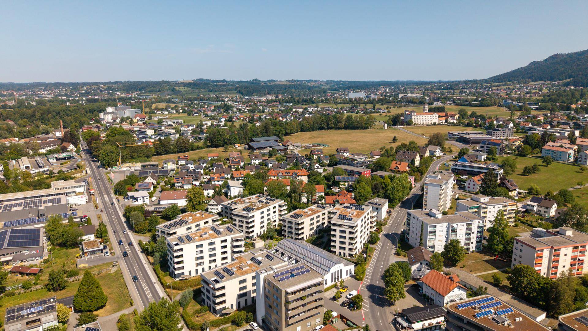 Luftaufnahme einer Wohnsiedlung mit modernen Gebäuden und grüner Umgebung unter blauem Himmel.