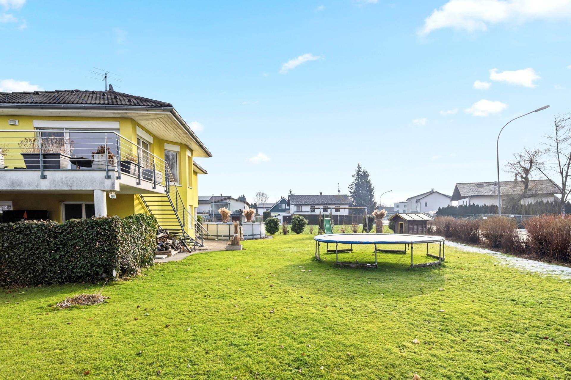 Großer grüner Garten mit Trampolin, Spielplatz und Einfamilienhaus.