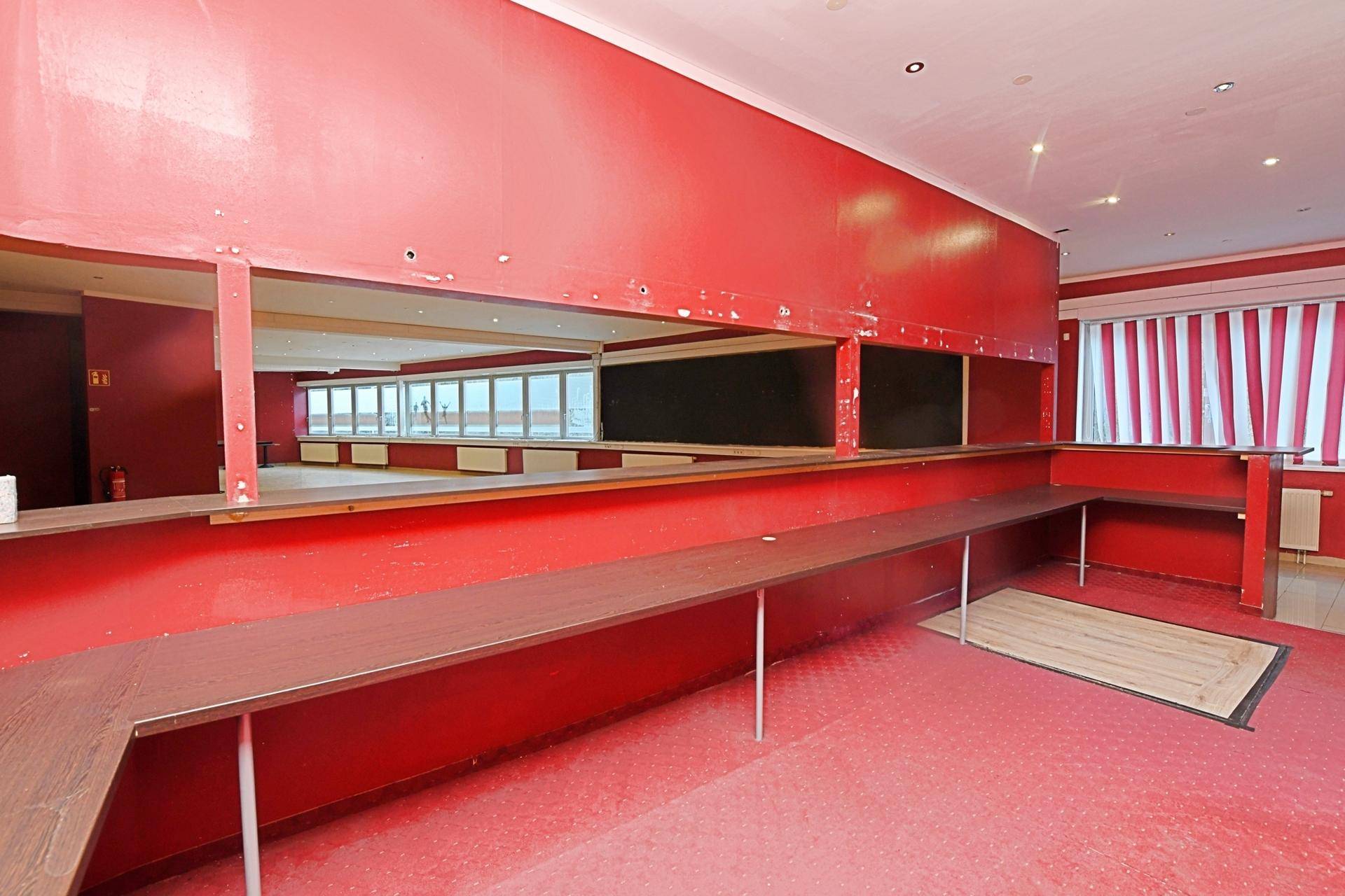 Roter Lounge-Bereich mit Teppichboden, Spiegeln und Blick auf die Fensterfront, bietet viel Platz.