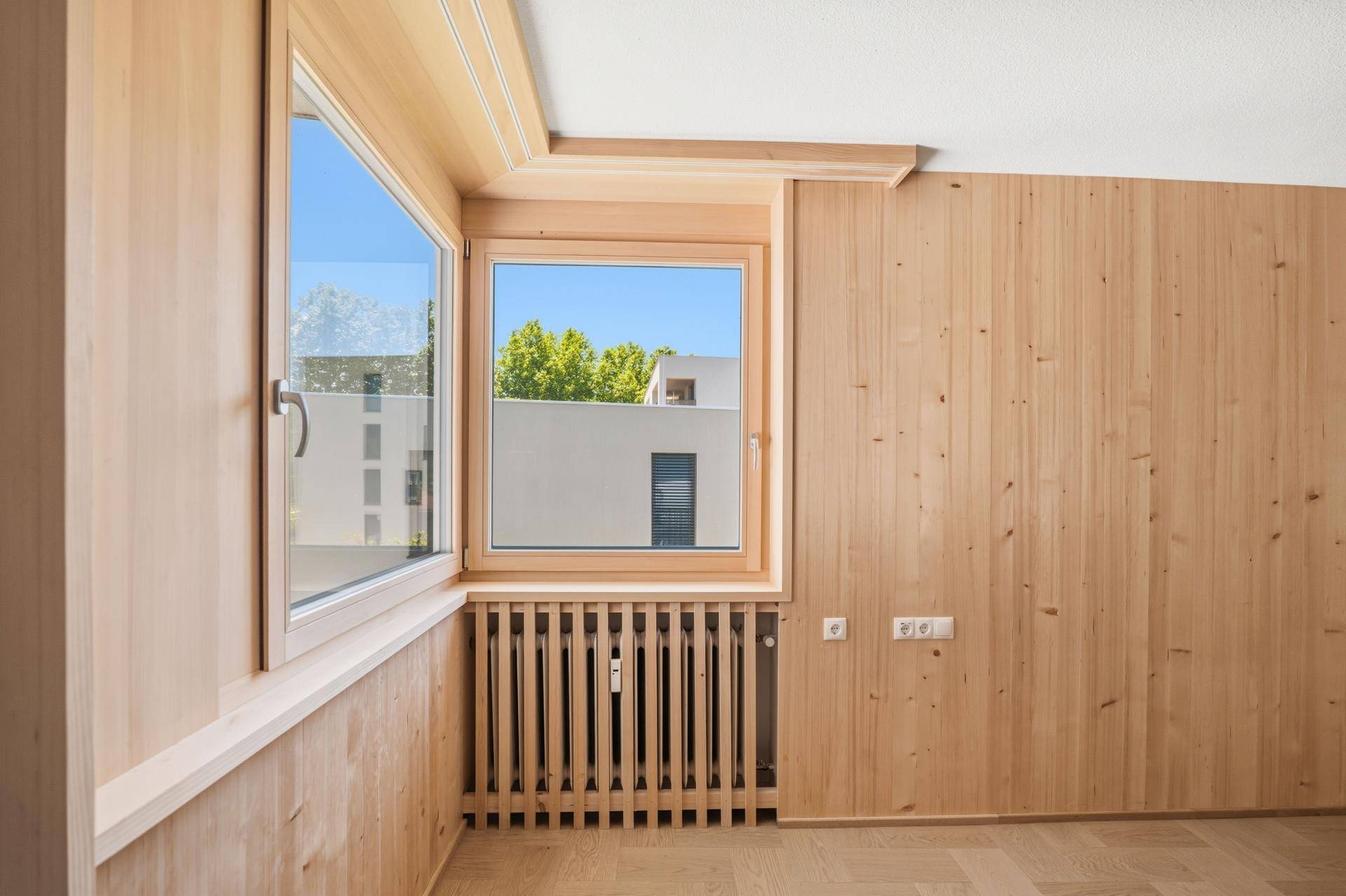 Detailansicht eines Fensters mit Holzrahmen und Holzverkleidung in einem hellen Raum.