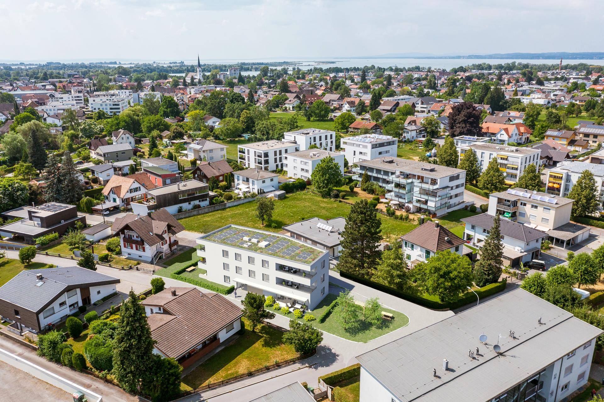 Luftaufnahme des neuen Wohngebäudes in einer grünen Wohngegend mit Seeblick im Hintergrund.