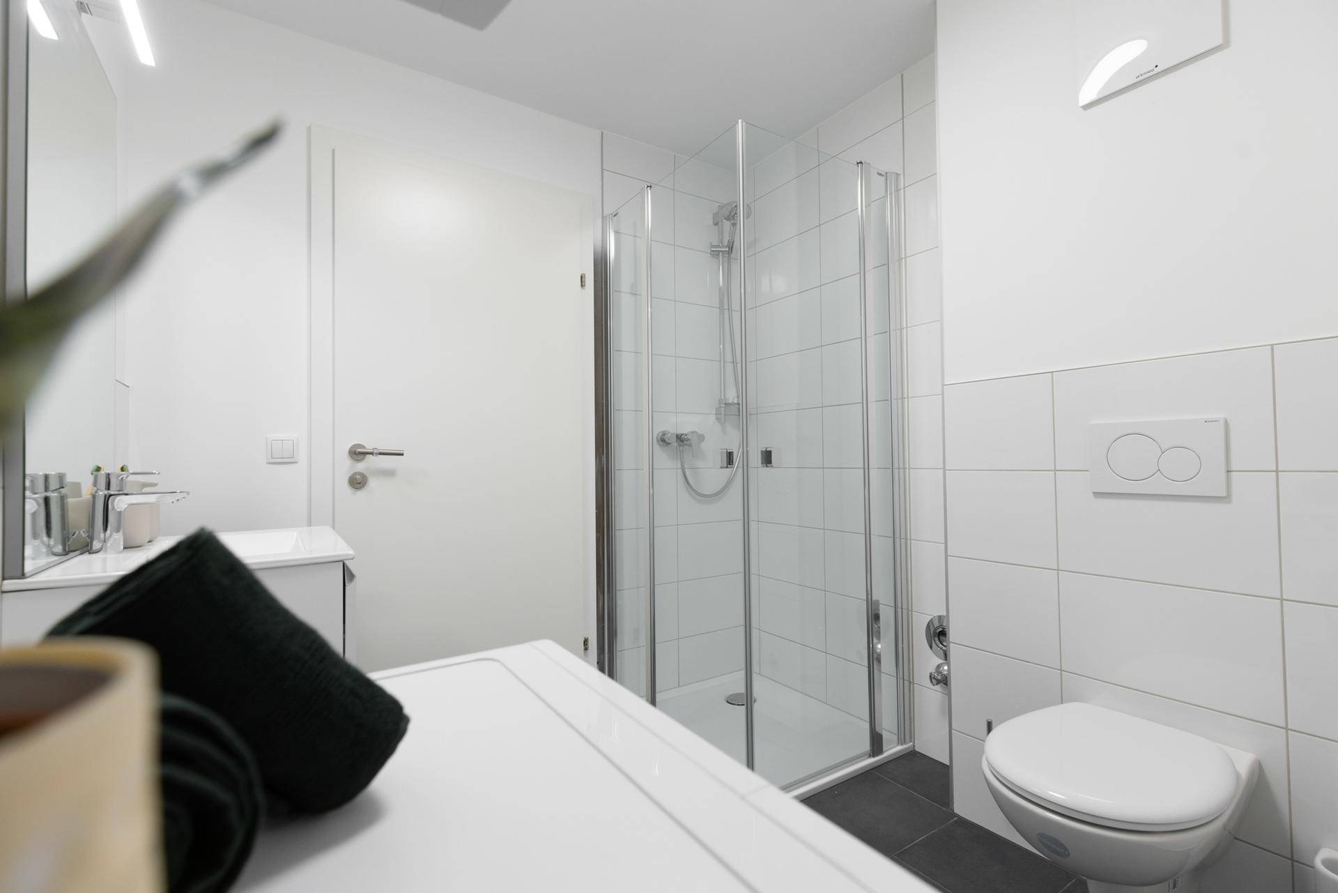 Modernes Badezimmer mit Duschkabine, wandhängendem WC und Waschtisch, hell gefliest.