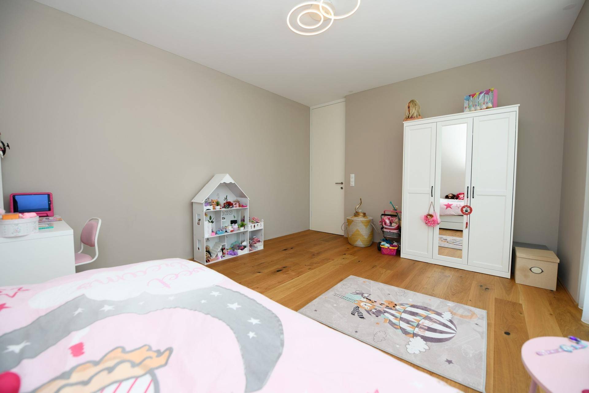 Kinderzimmer mit Holzboden, weißem Kleiderschrank und Spielzeug.
