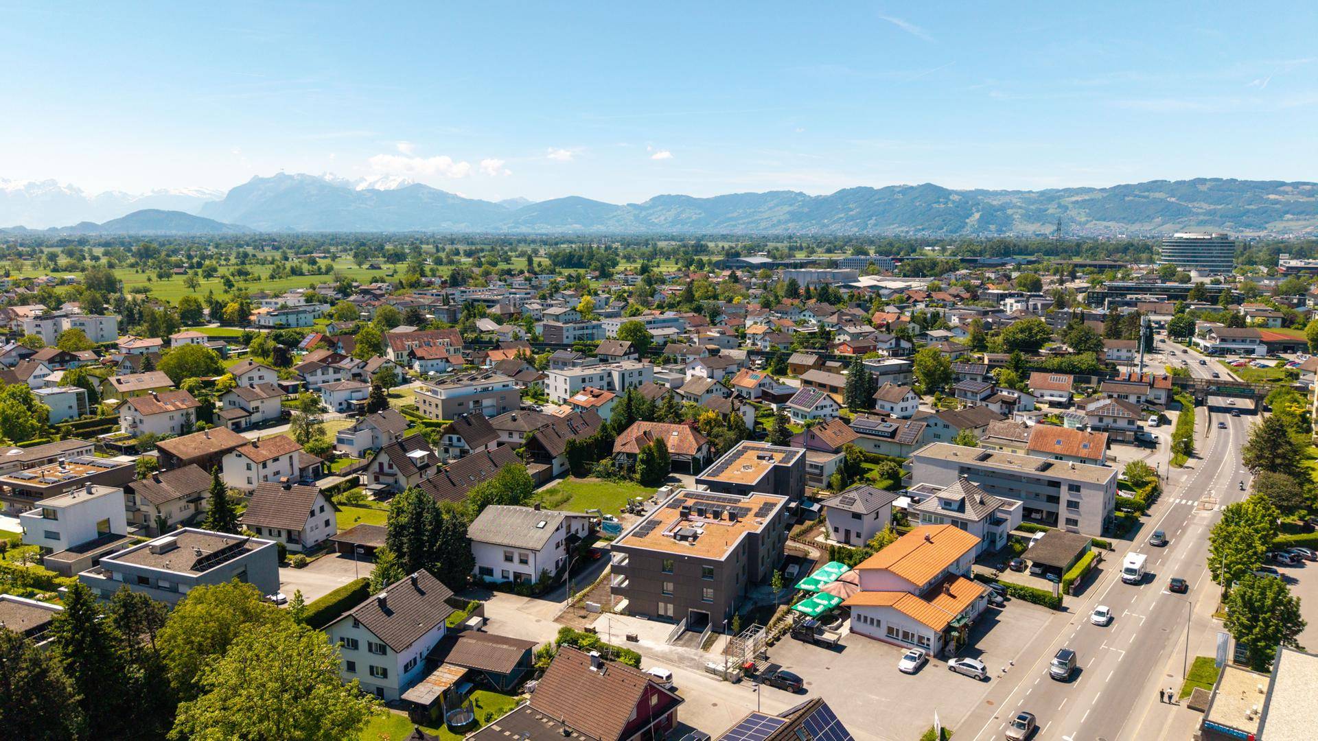 Weitläufige Luftaufnahme einer Wohngegend mit Bergen im Hintergrund unter blauem Himmel.