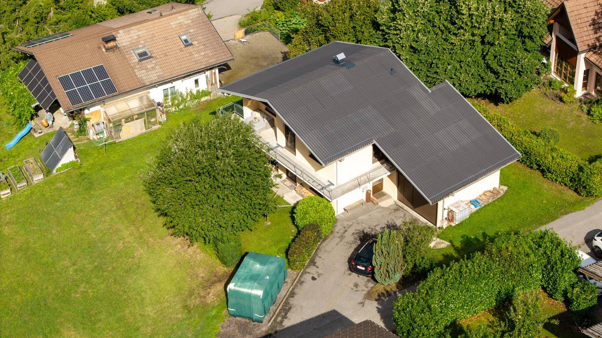 Vogelperspektive eines Wohnhauses mit dunklem Dach, Garage und gepflegtem Gartenbereich.
