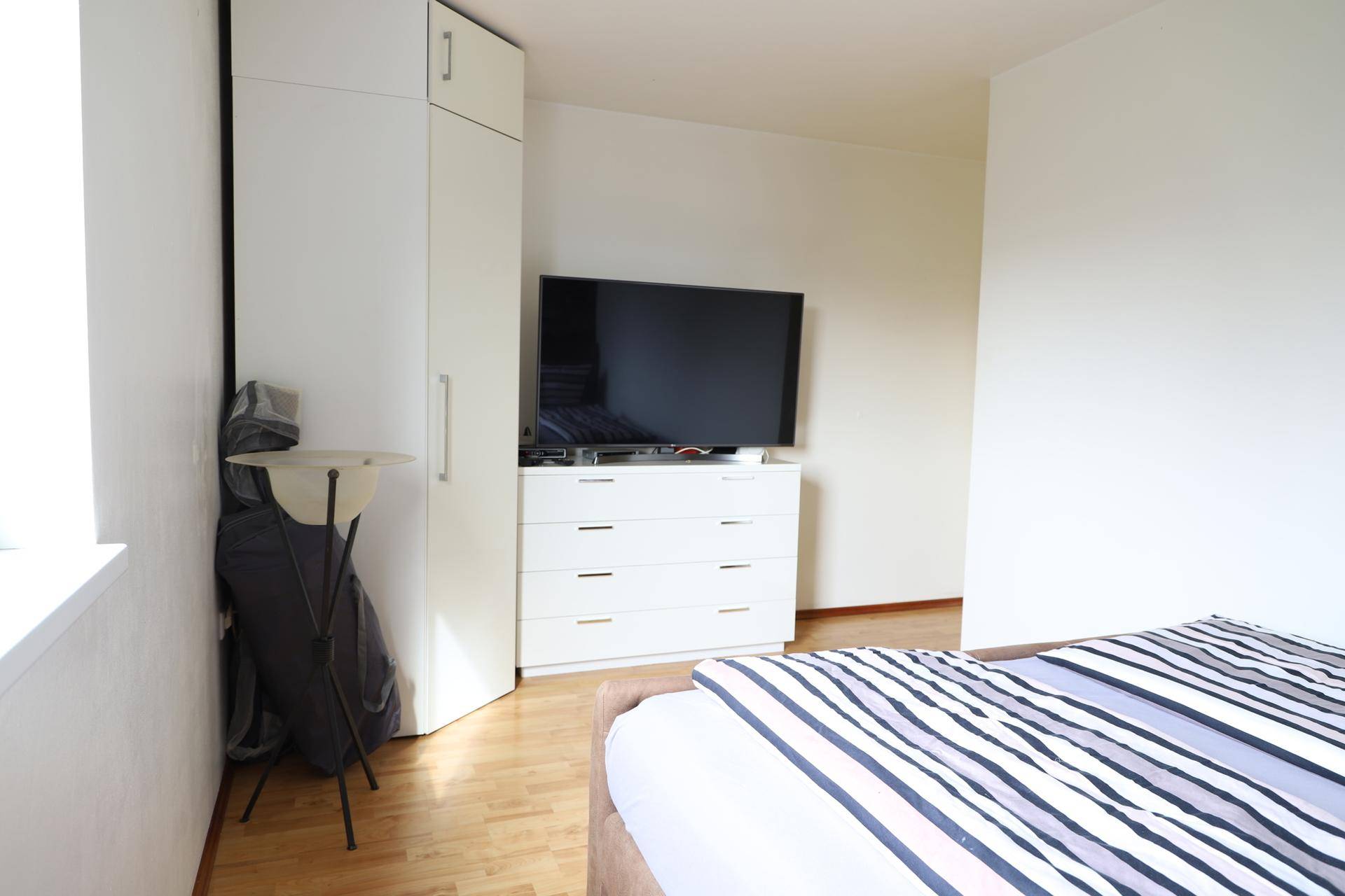 Schlafzimmer mit Holzboden, weißer Kommode, Fernseher und praktischem Kleiderschrank.