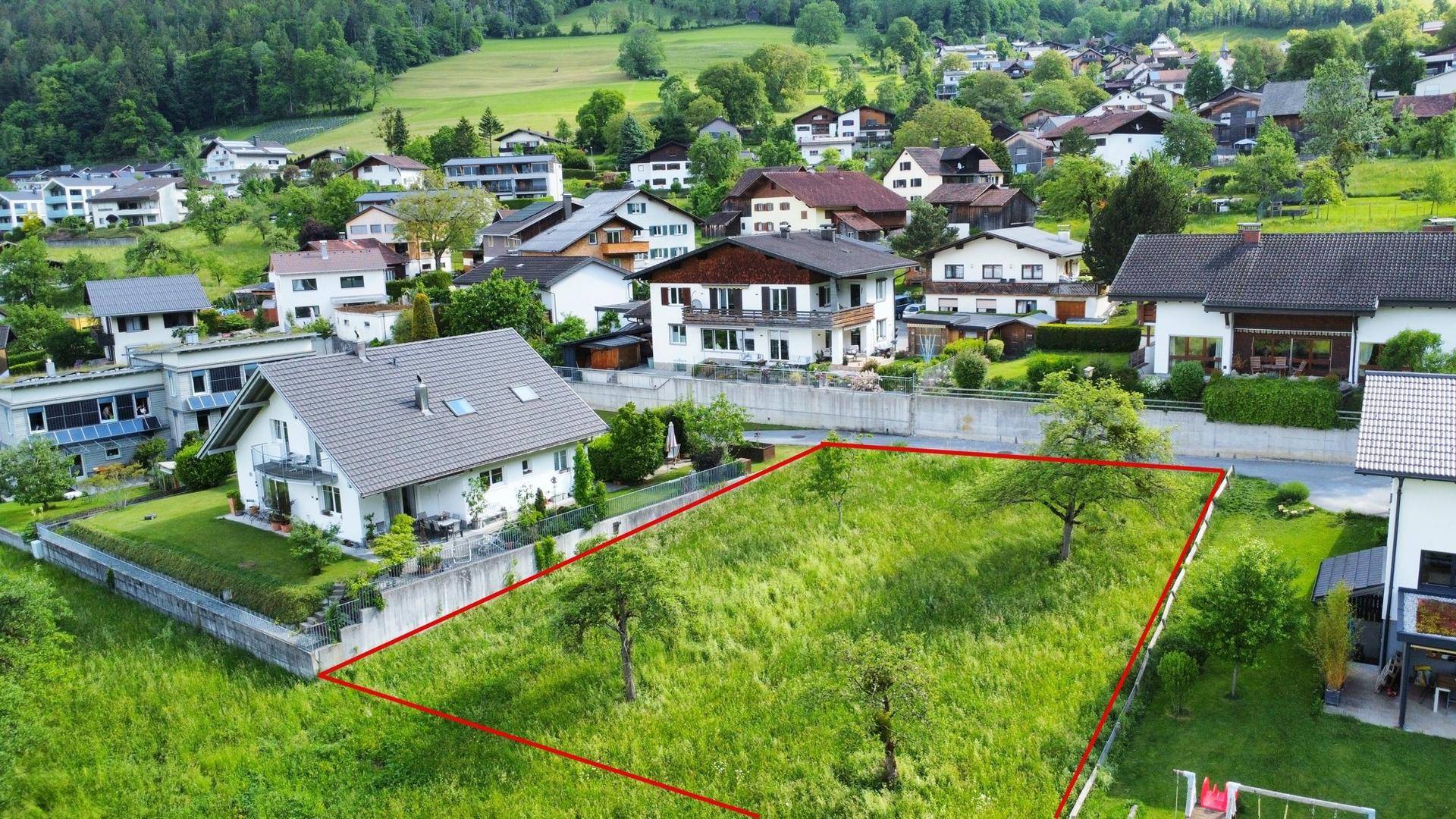 Luftaufnahme eines Baugrundstücks mit roter Umrandung, umgeben von Einfamilienhäusern in grüner Wohnlage.